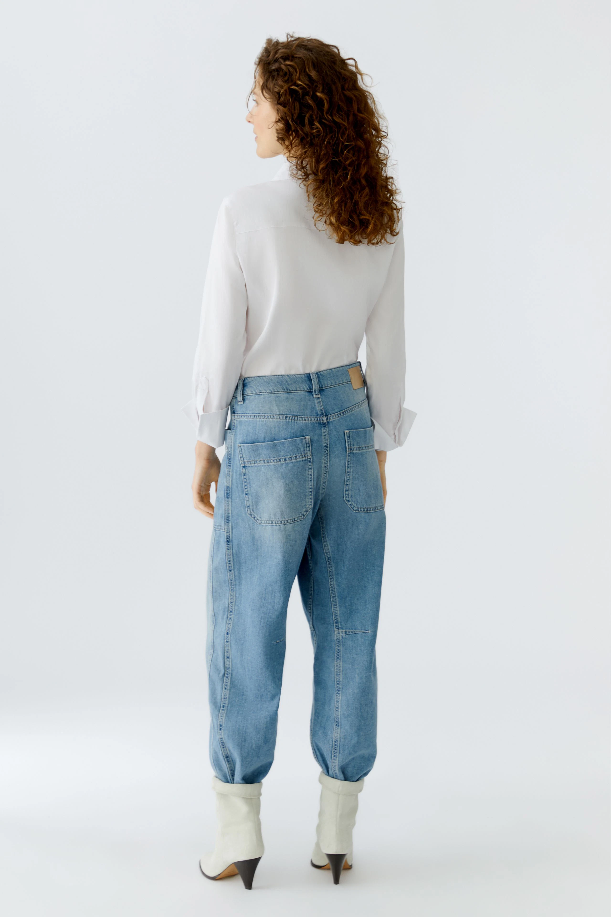 Damen Jeans Barrel: Frau mit lockigen Haaren trägt lässige, hellblaue Jeans mit weitem Schnitt.