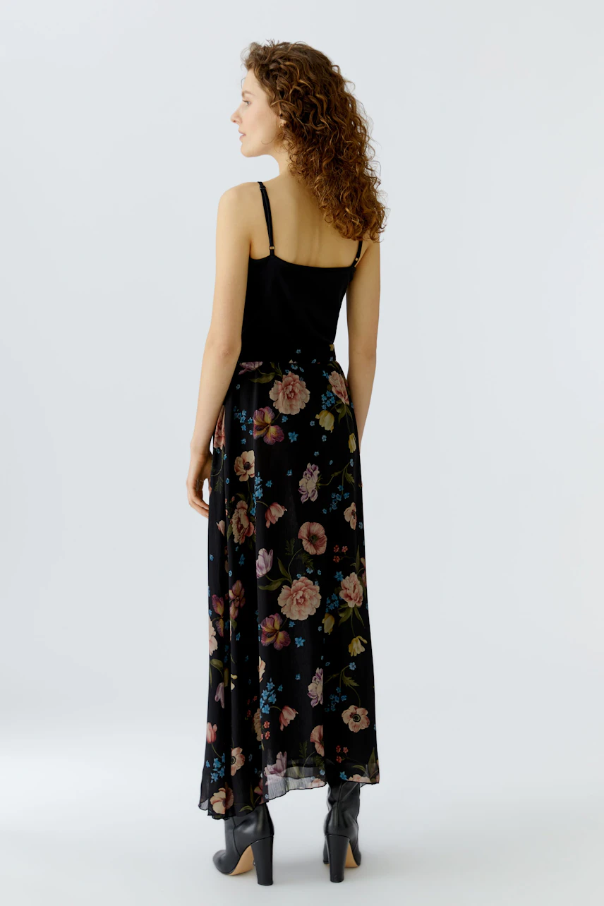 Maxi skirt: Woman in a floral black maxi skirt with a fitted top, showcasing a relaxed style.