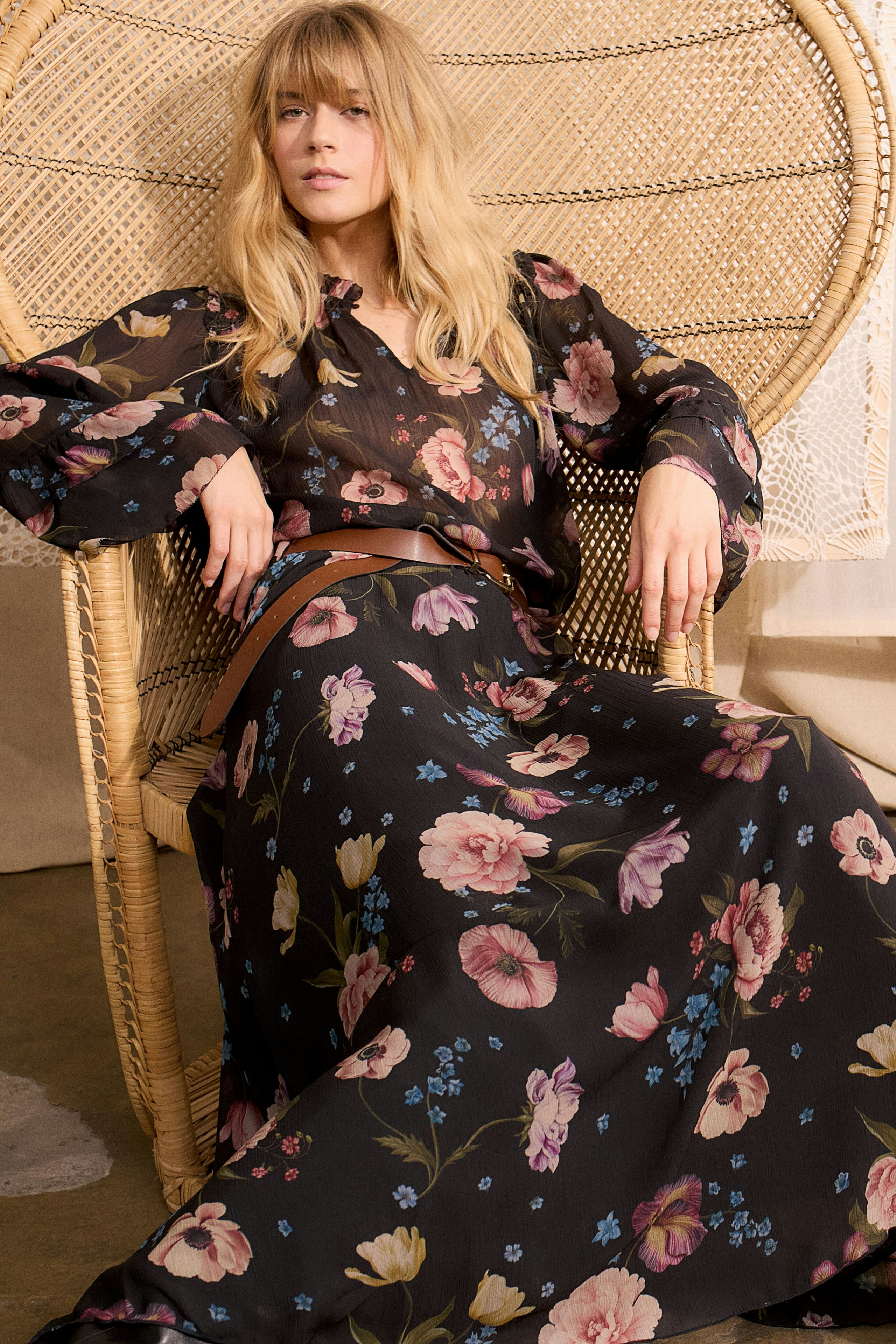 Floral maxi skirt: Woman in a black skirt with colorful flowers, sitting comfortably in a chair.