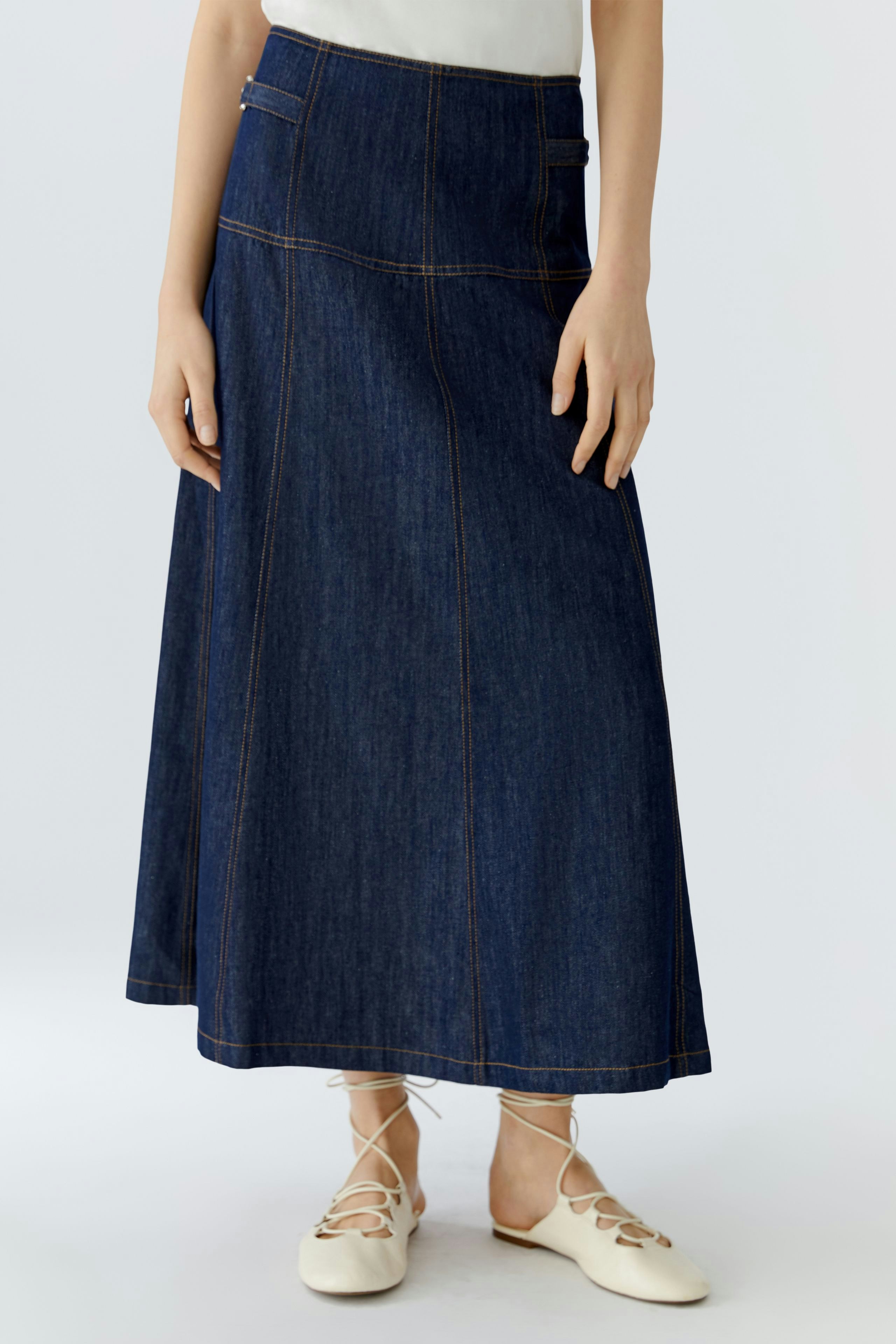 Denim A-line skirt: Woman in a long, dark blue skirt with a fitted waist and casual style.