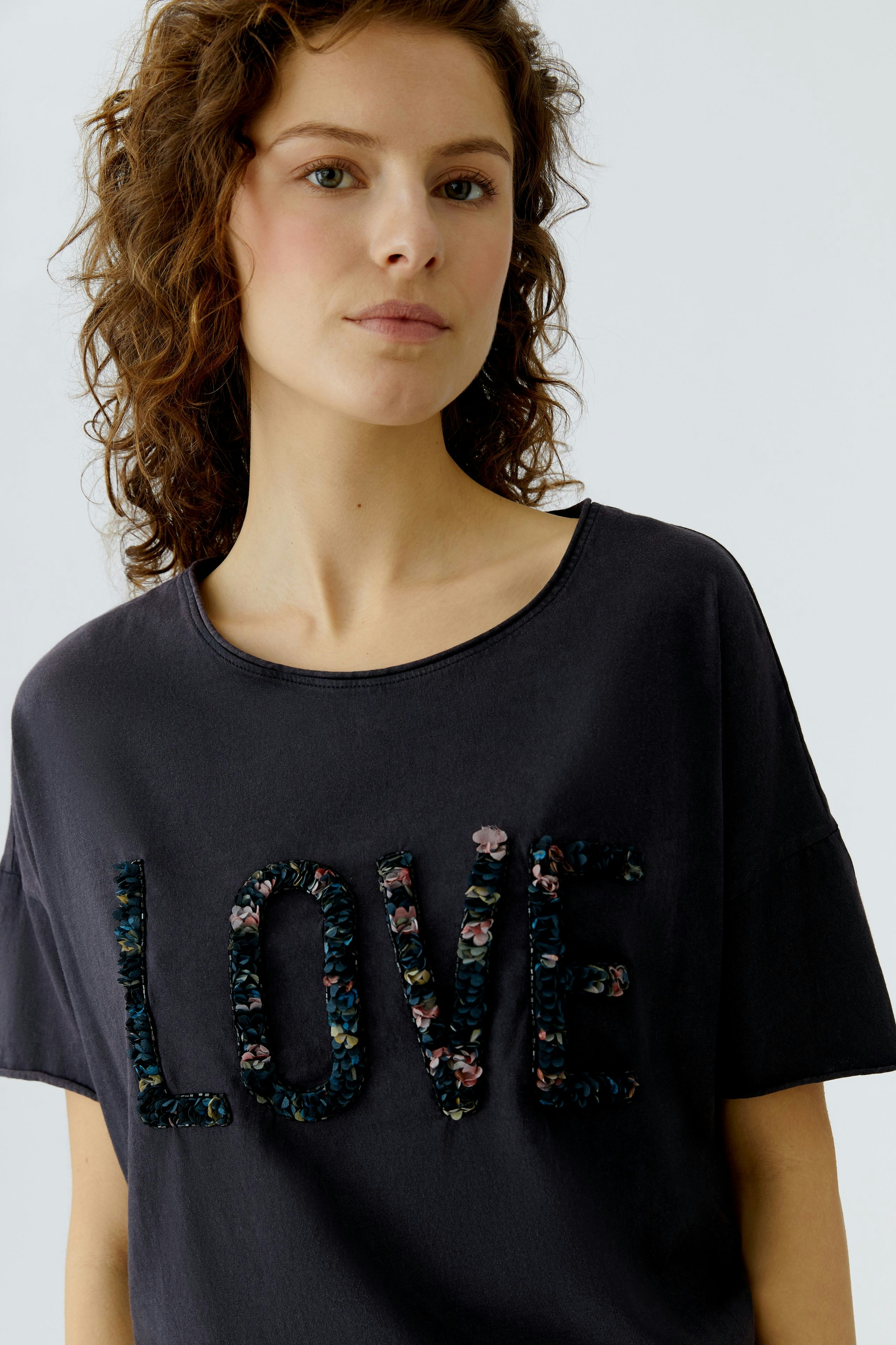 Casual women's T-shirt: Young woman in a dark shirt with floral 'LOVE' lettering, exuding a relaxed vibe.