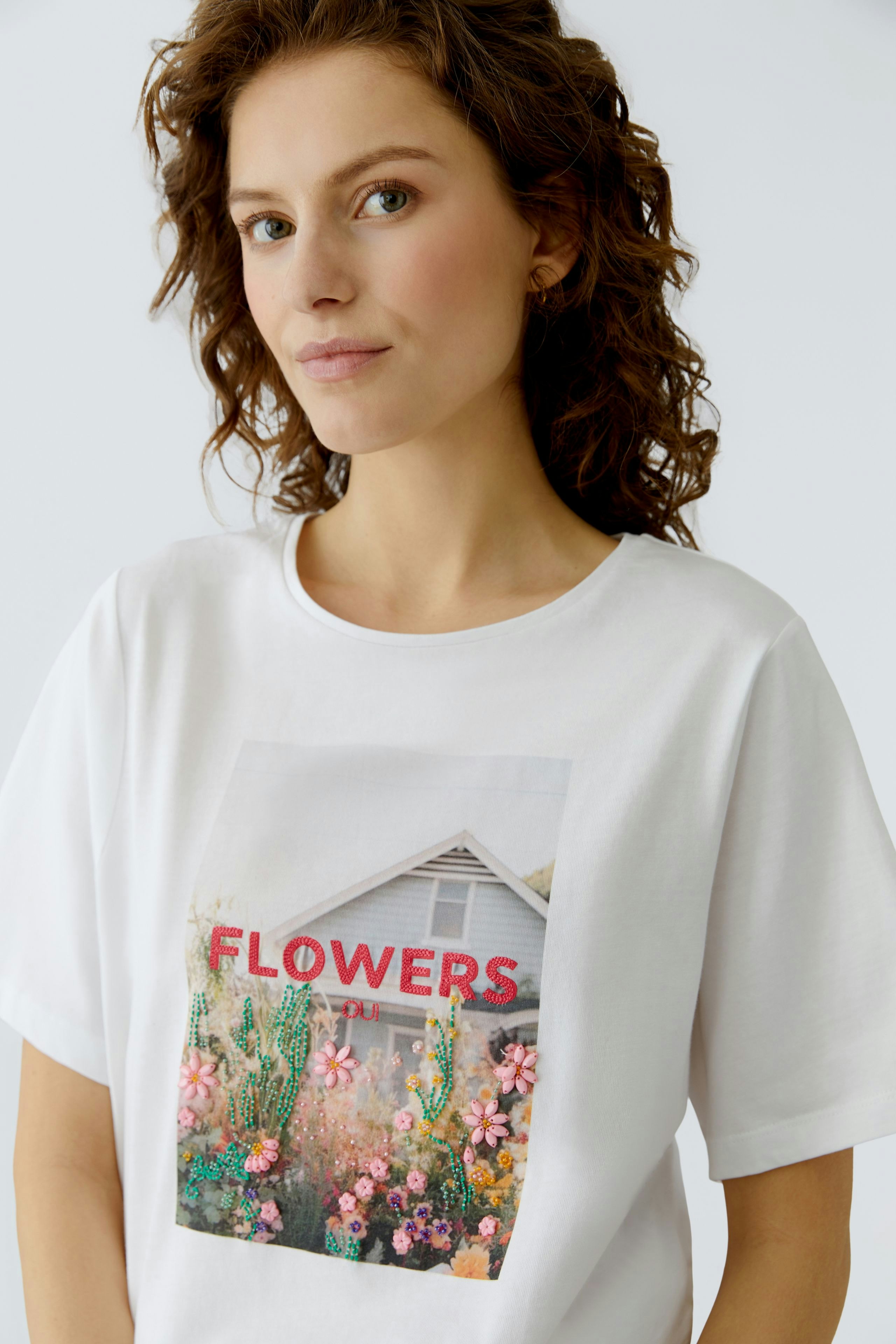 Casual women's T-shirt: Woman in a white tee featuring a colorful floral print and the word 'FLOWERS'.