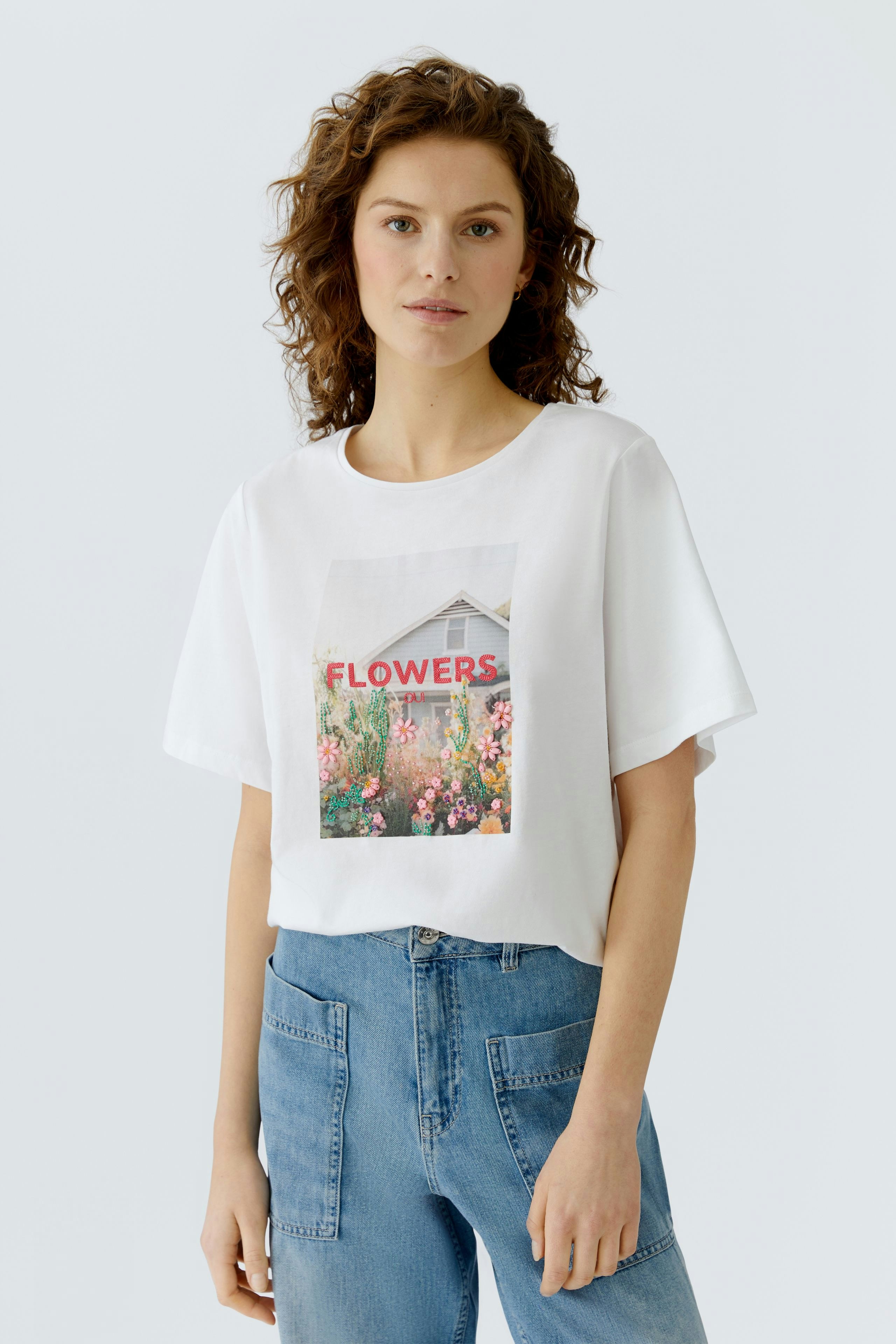 Casual women's T-shirt: Young woman in a white tee with a floral print, paired with blue jeans.