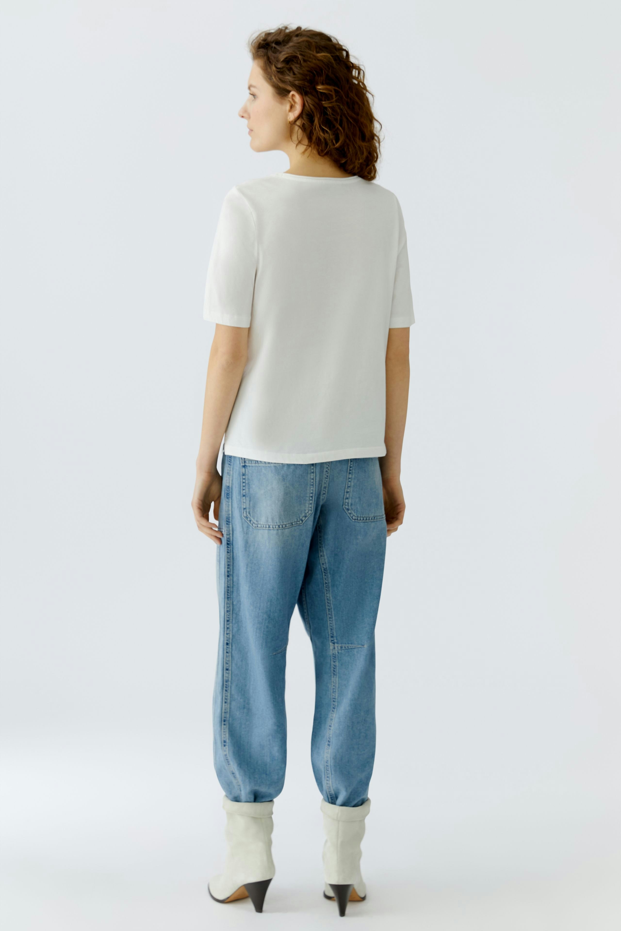 Casual women's T-shirt: A woman in a white short-sleeve top paired with relaxed-fit jeans.