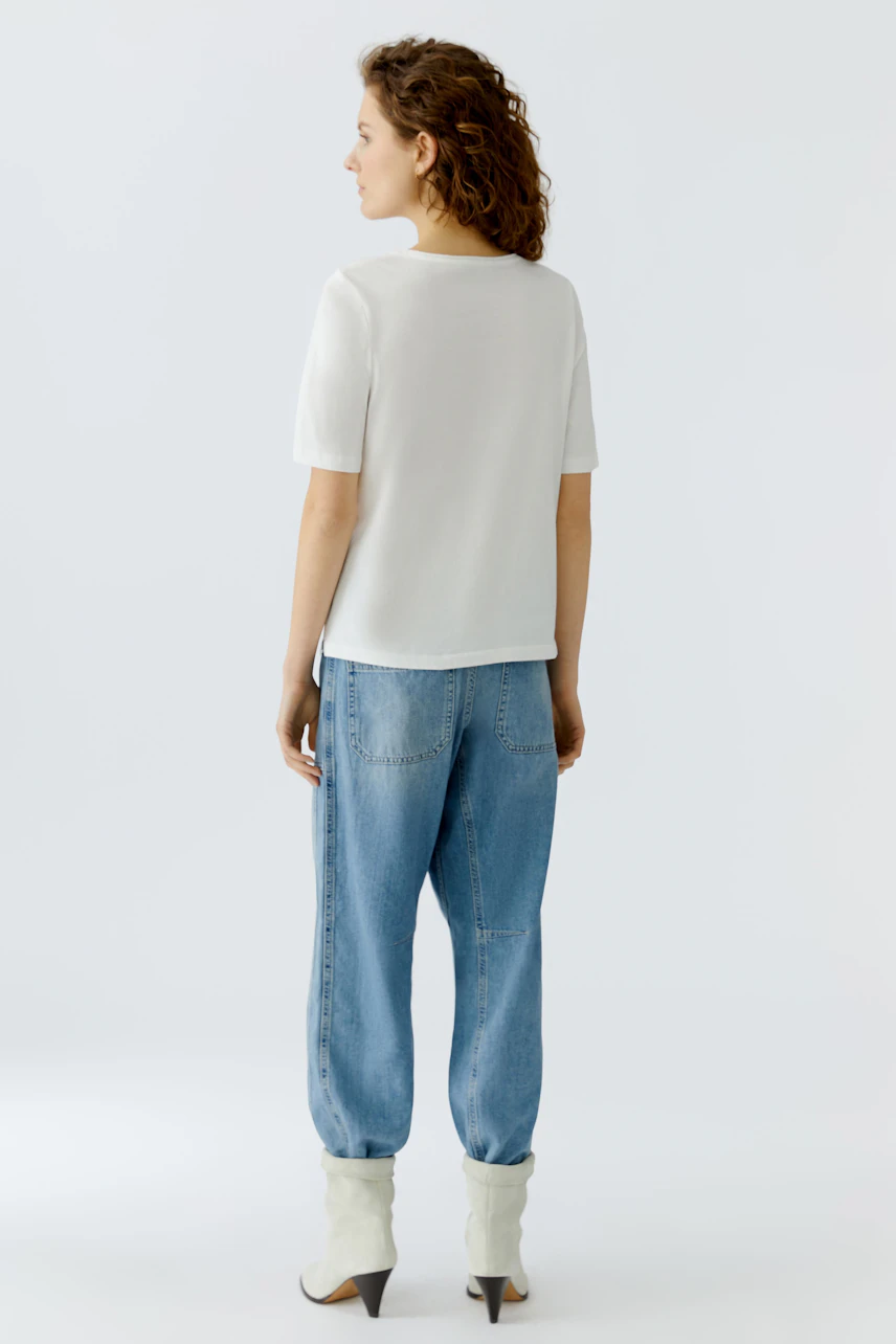 Casual women's T-shirt: A woman in a white short-sleeve top paired with relaxed-fit jeans.