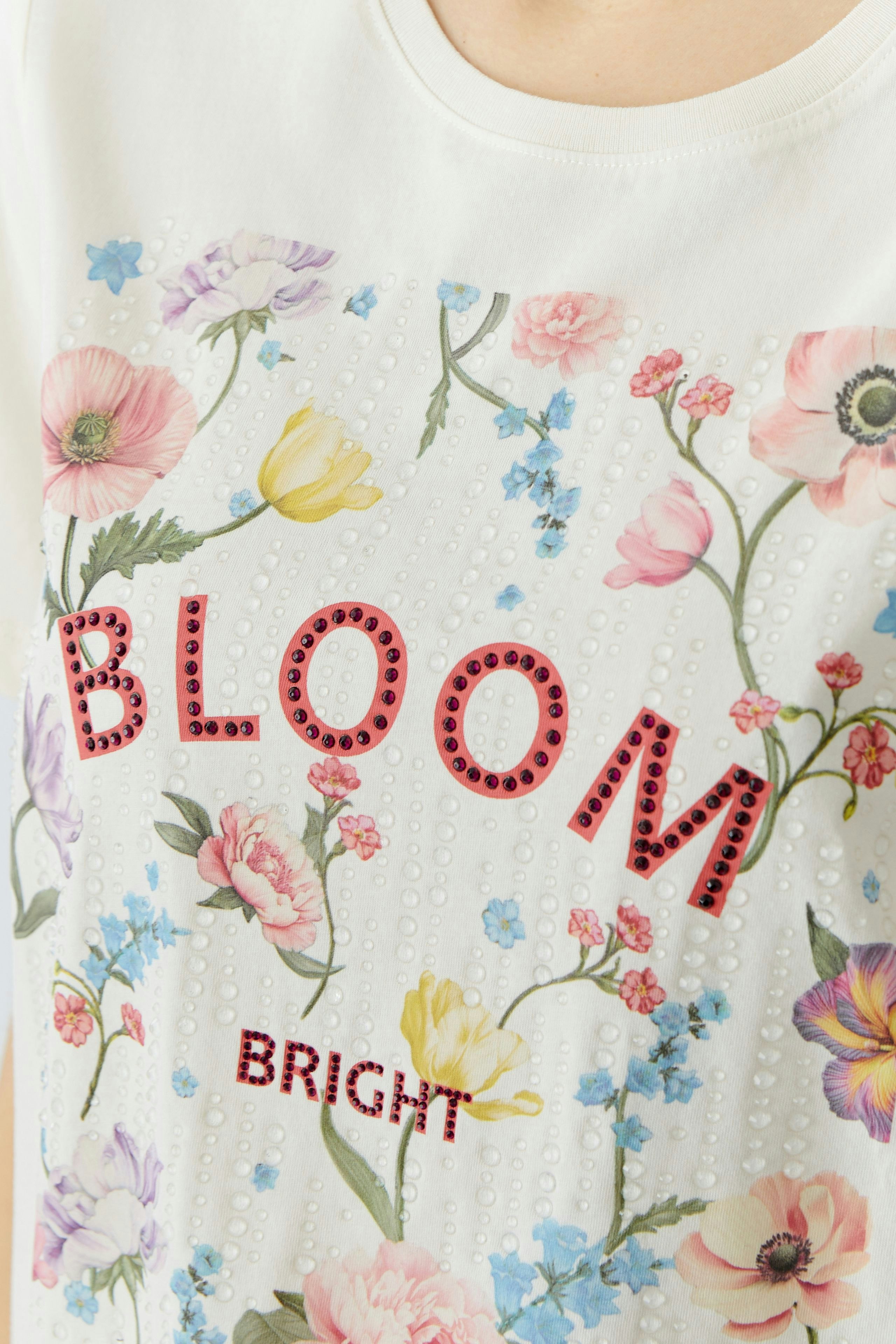 Casual women's T-shirt: Close-up of a woman wearing a white tee with floral print and 'BLOOM BRIGHT' text.