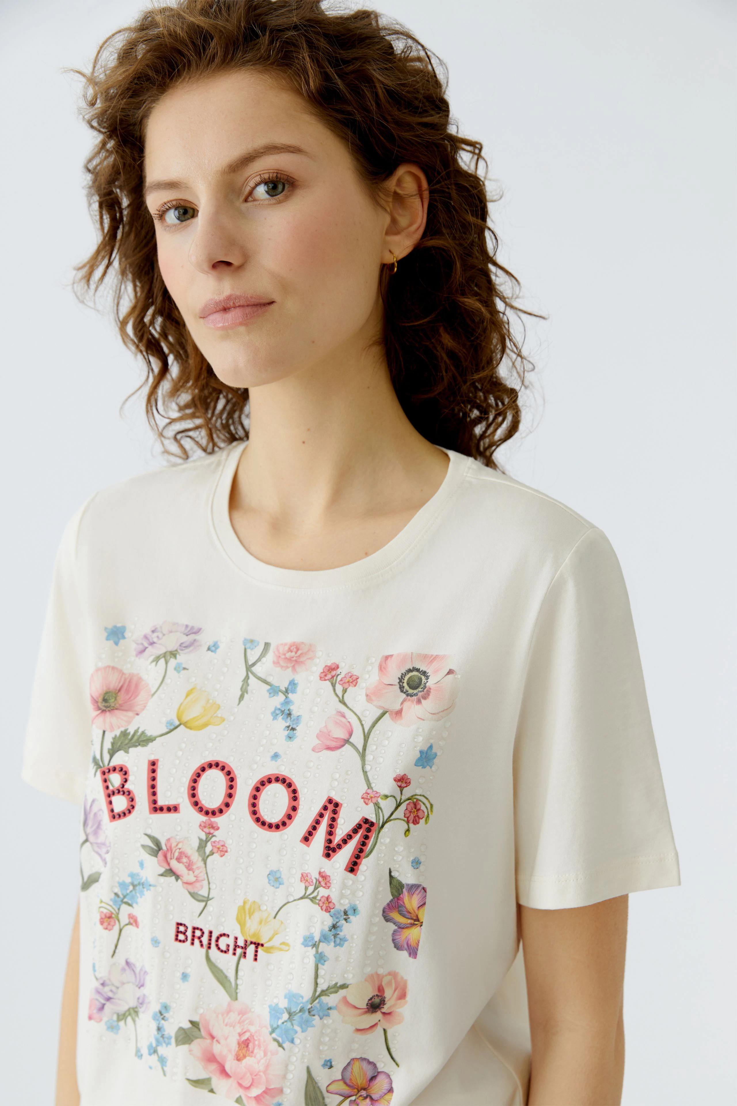 Casual women's T-shirt: Young woman in a cream shirt with floral print and 'BLOOM BRIGHT' text.