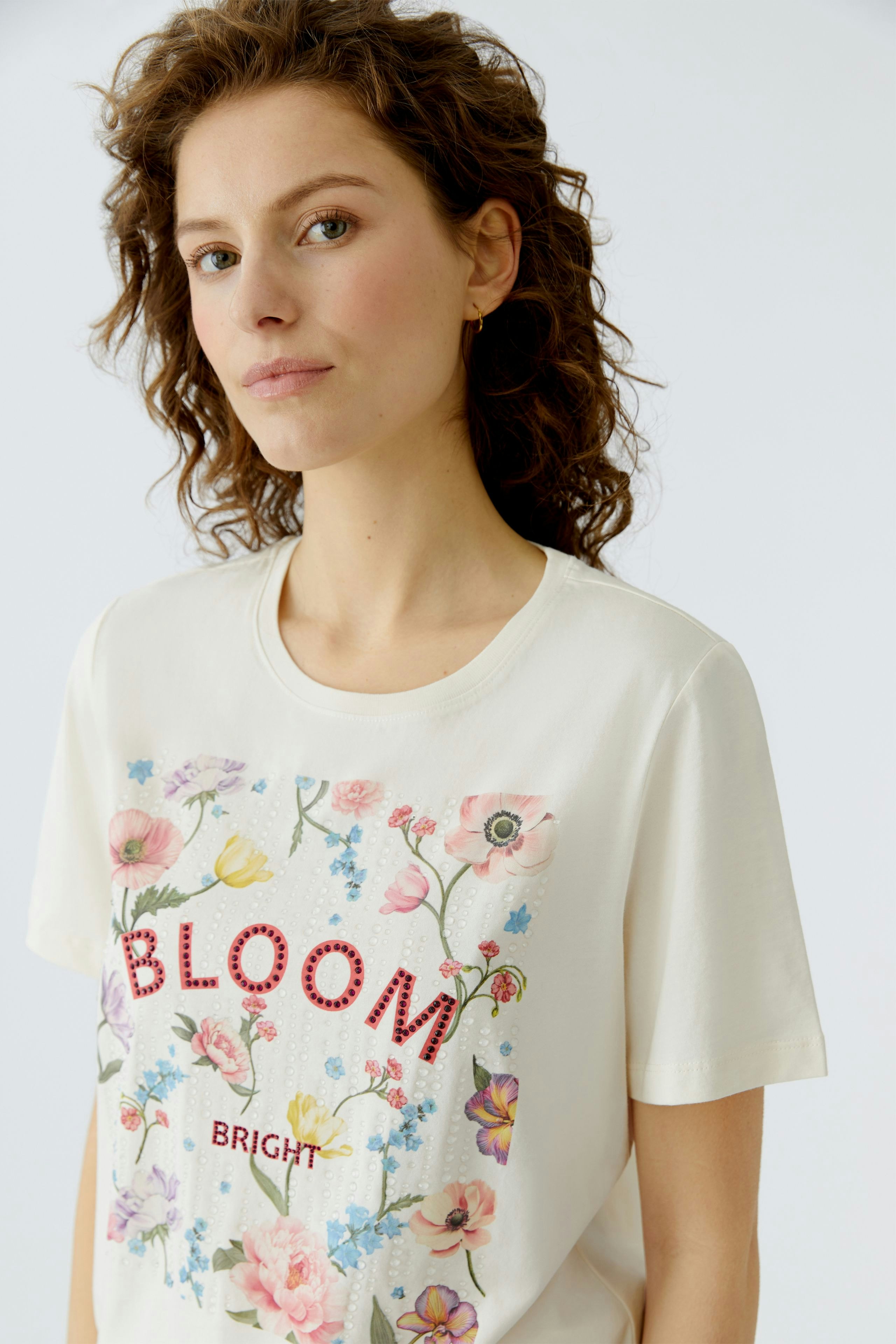 Casual women's T-shirt: Young woman in a cream shirt with floral print and 'BLOOM BRIGHT' text.