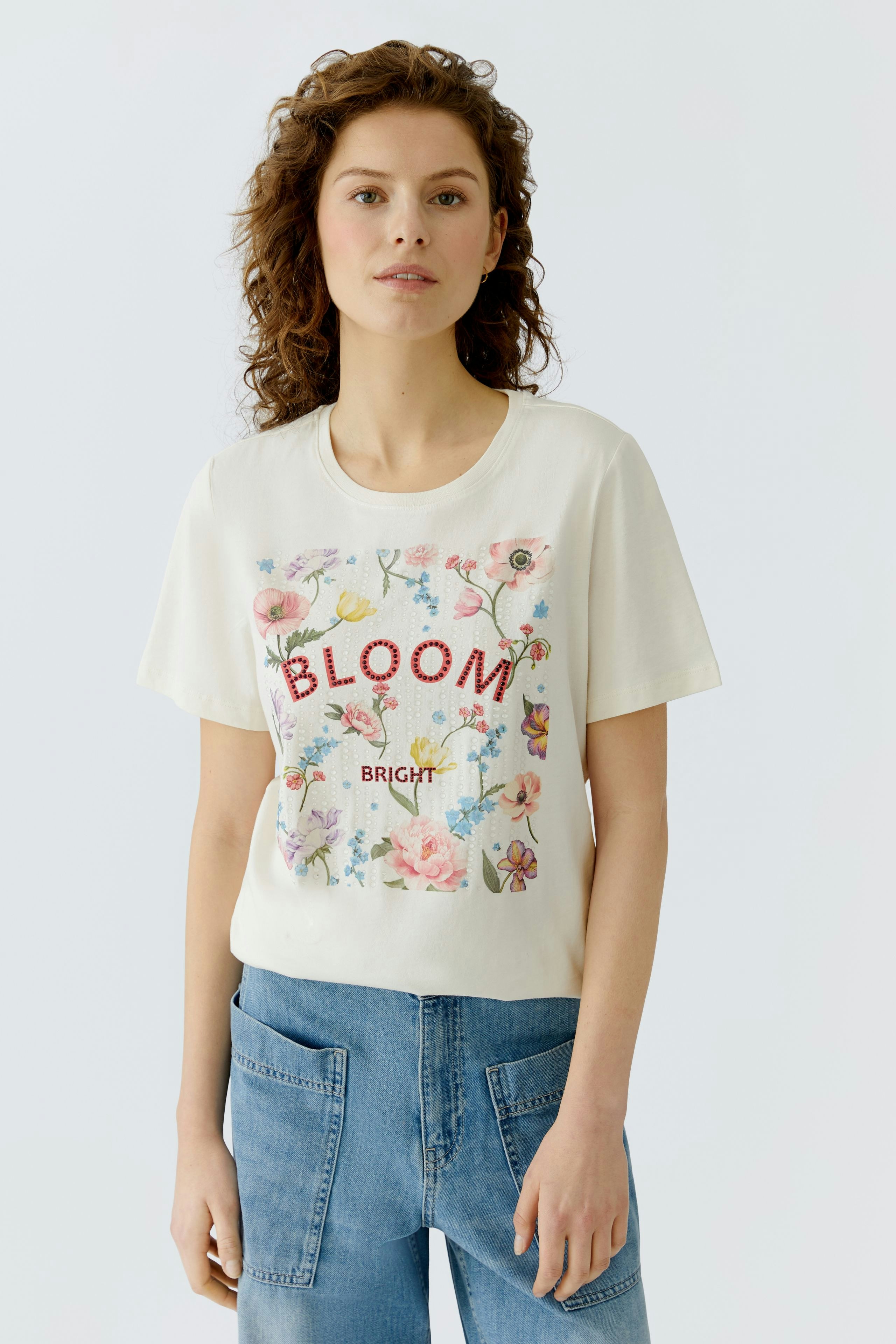 Casual women's T-shirt: Young woman in a light shirt with floral print and 'BLOOM' text.