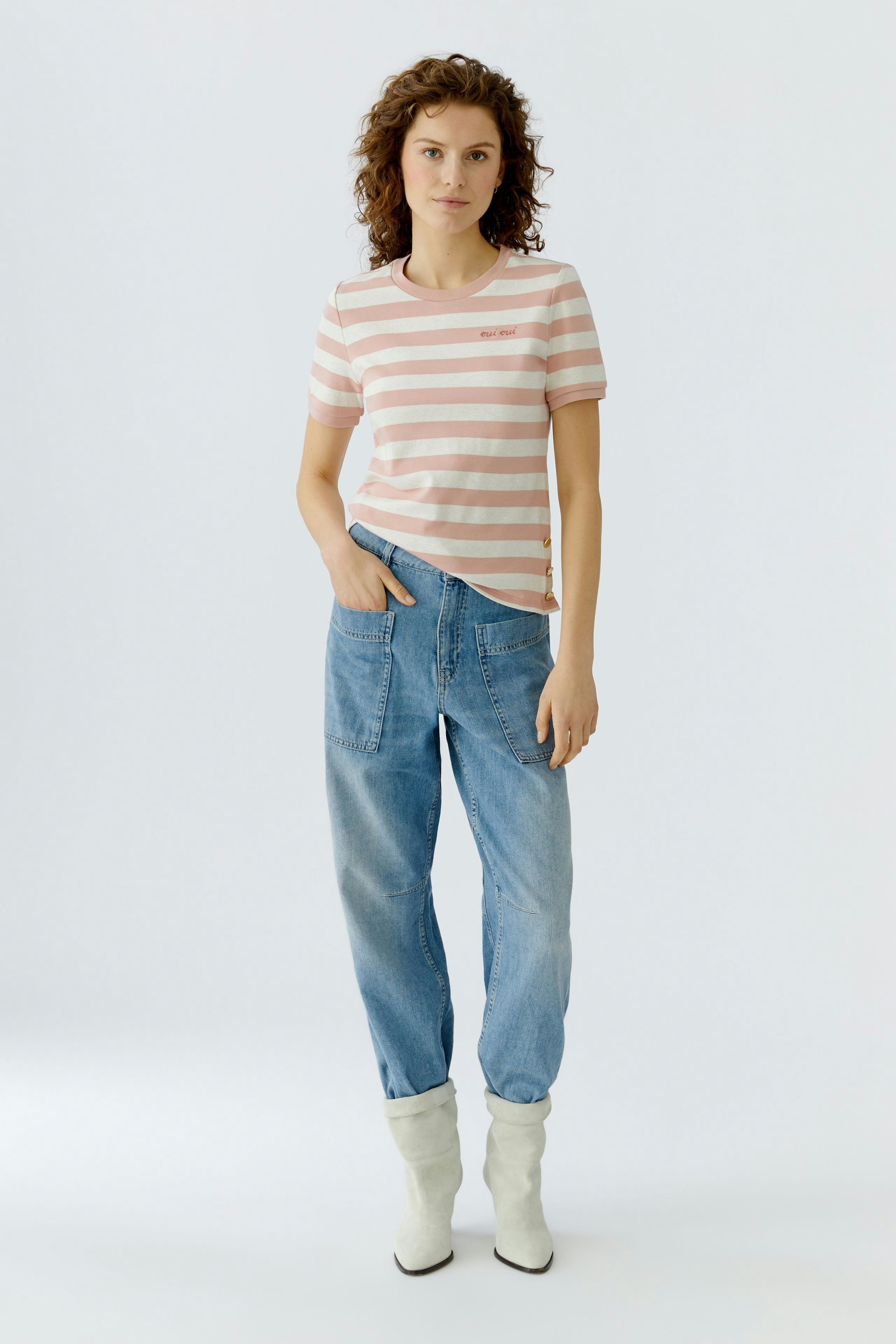 Casual women's T-shirt: Young woman in a striped pink and white tee with relaxed fit jeans.