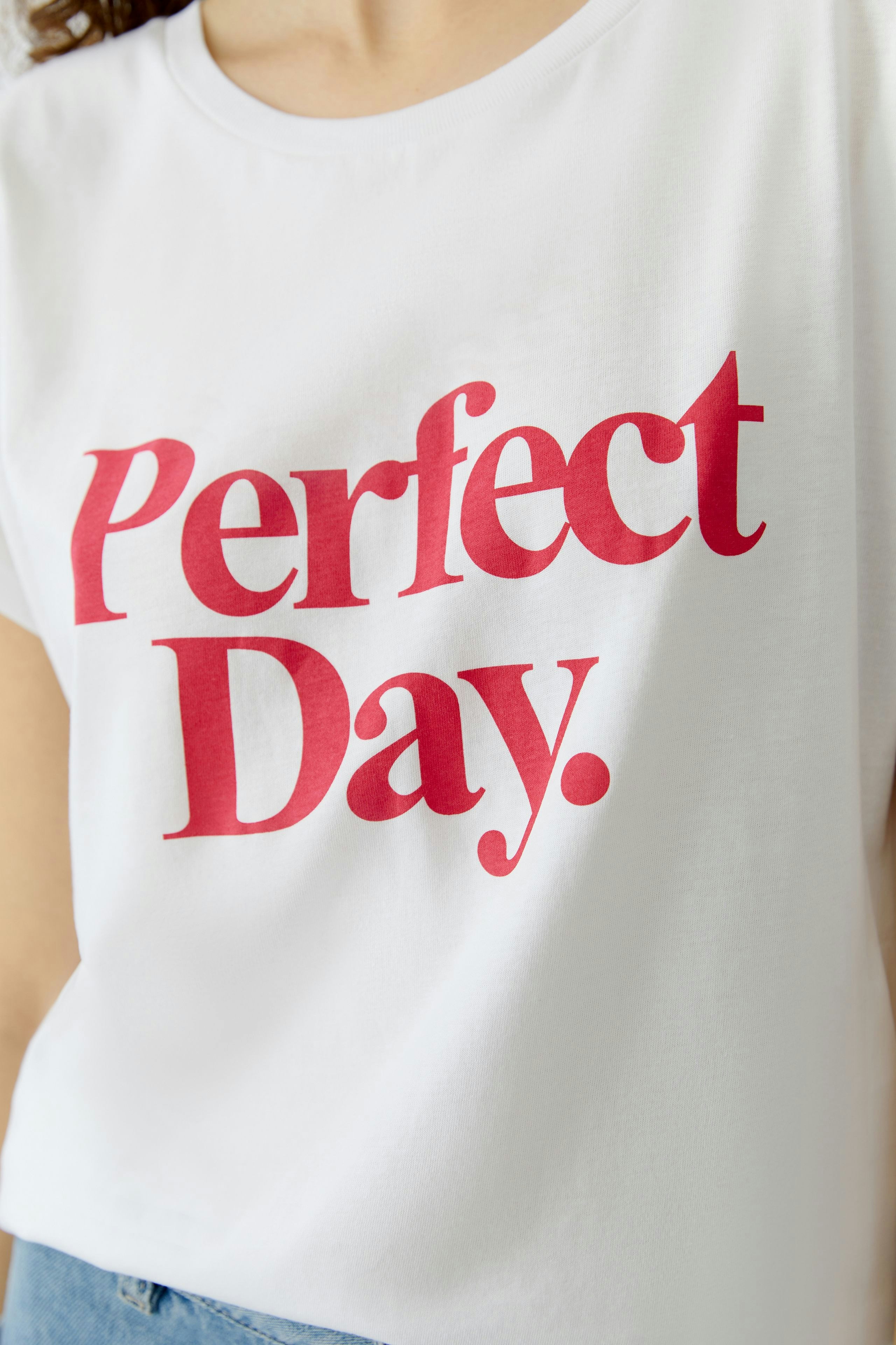 Casual women's T-shirt: Close-up of a woman wearing a white tee with 'Perfect Day' in bold red letters.
