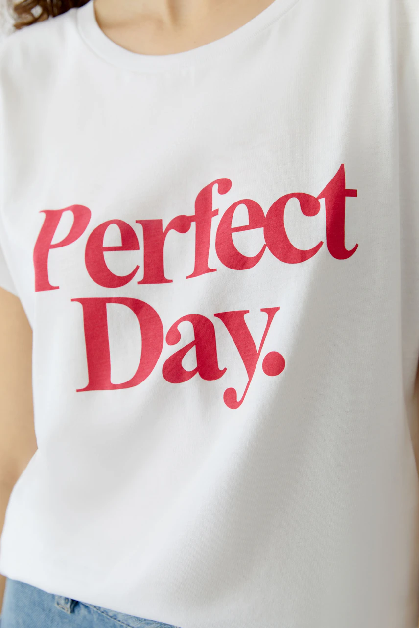 Casual women's T-shirt: Close-up of a woman wearing a white tee with 'Perfect Day' in bold red letters.