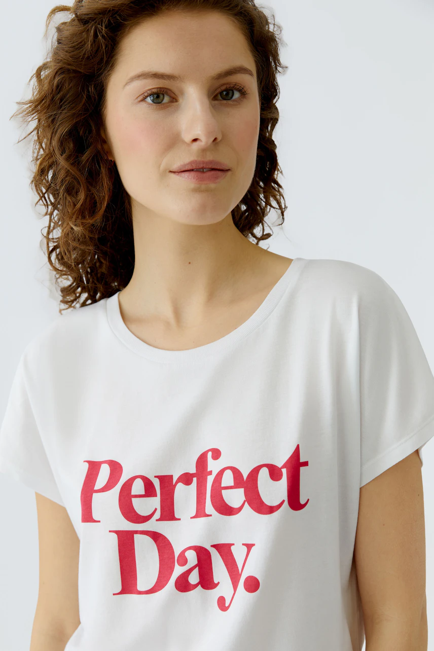 Casual women's T-shirt: Young woman in a white tee with 'Perfect Day.' print, smiling confidently.