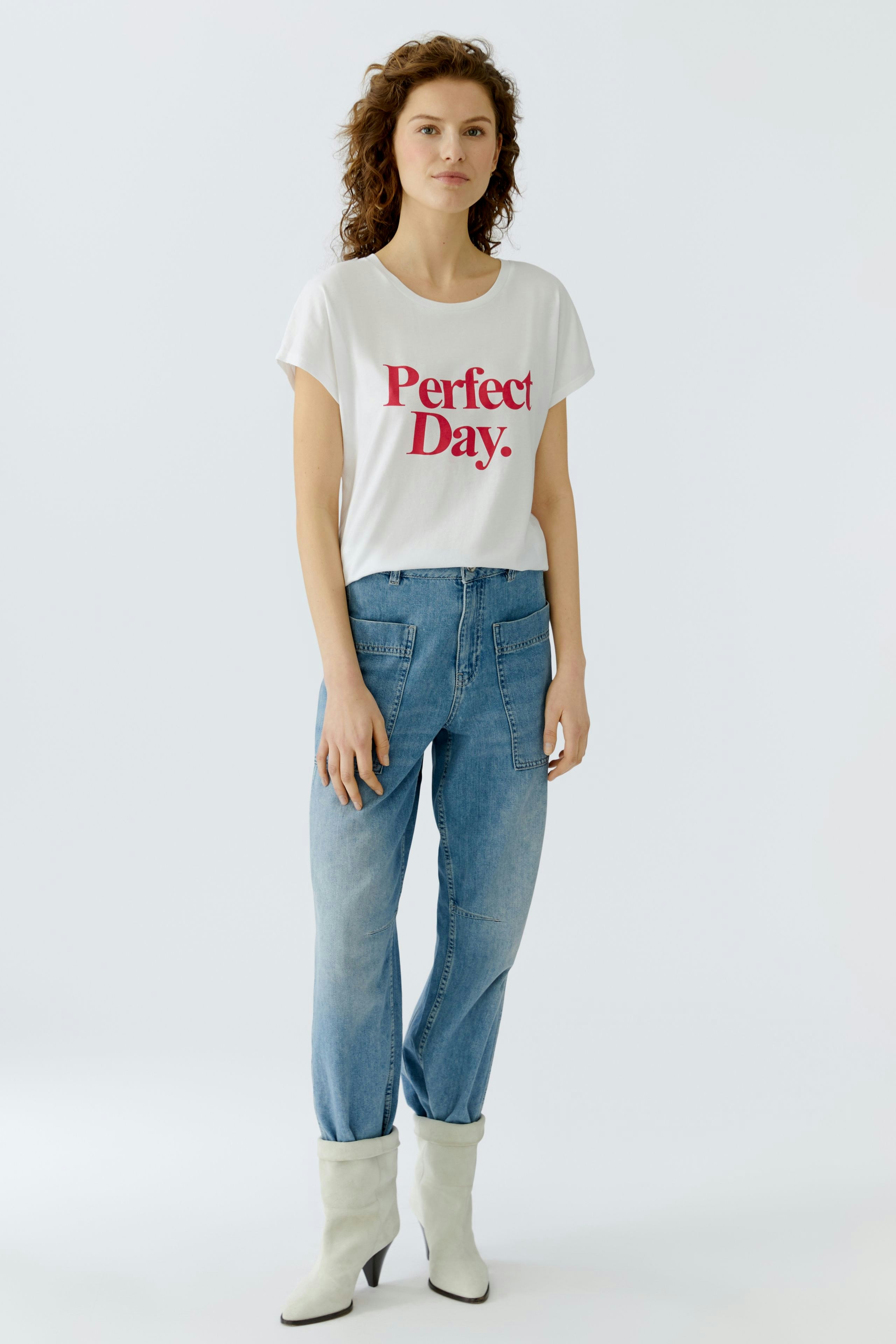 Casual women's T-shirt: Young woman in a white tee with 'Perfect Day.' print and relaxed jeans.