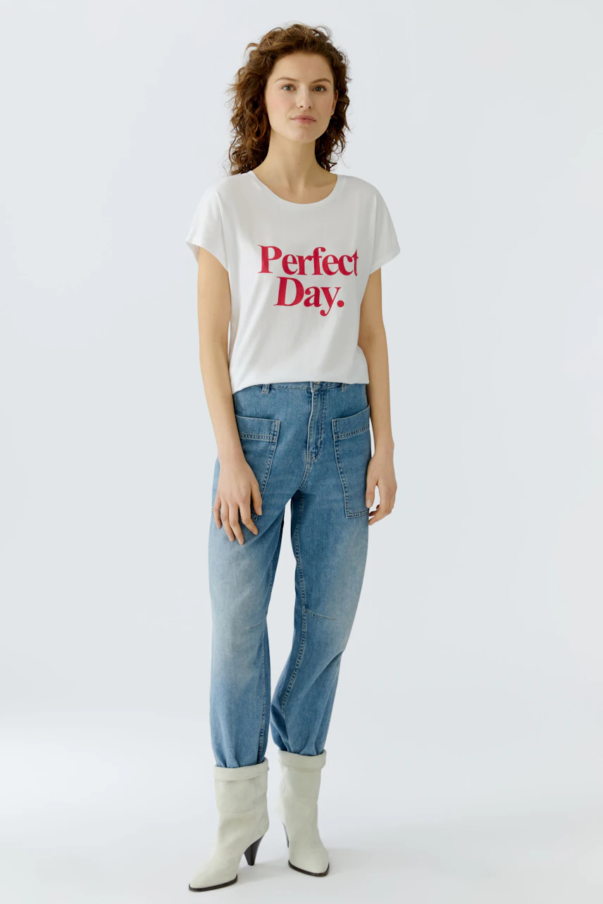 Casual women's T-shirt: Young woman in a white tee with 'Perfect Day.' print and relaxed jeans.