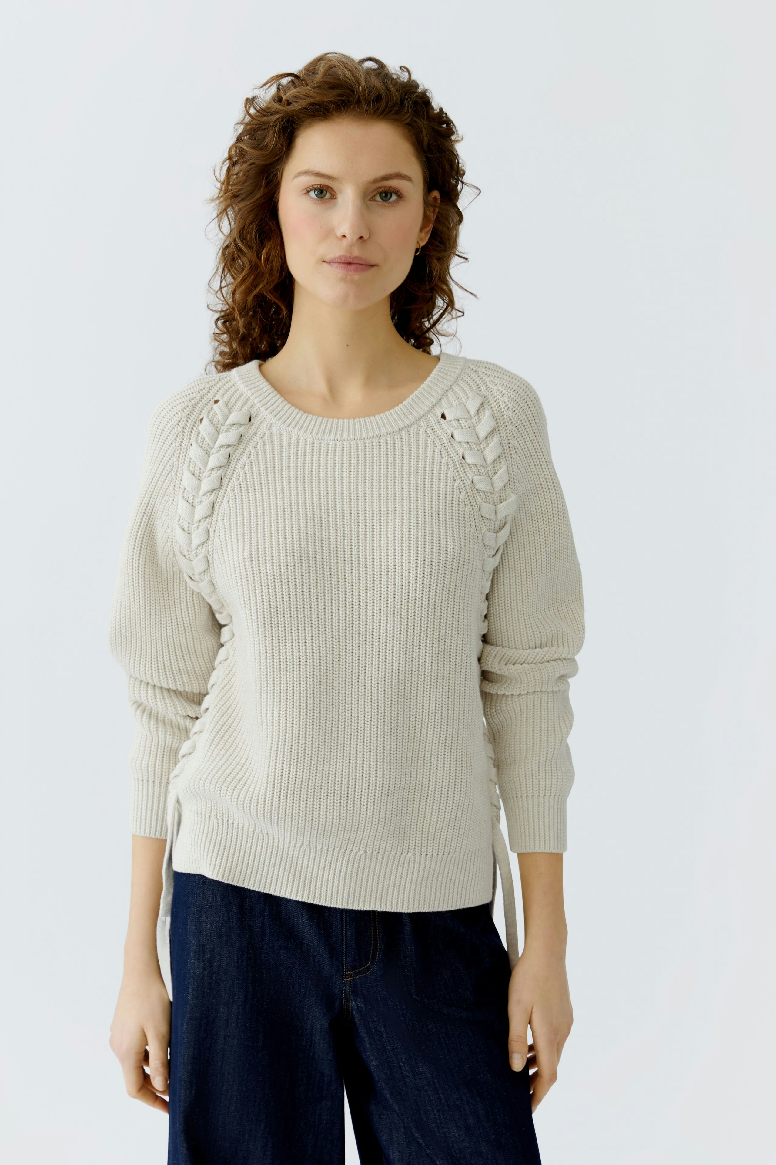 Casual women's pullover: A woman in a light beige ribbed pullover with unique side detailing.