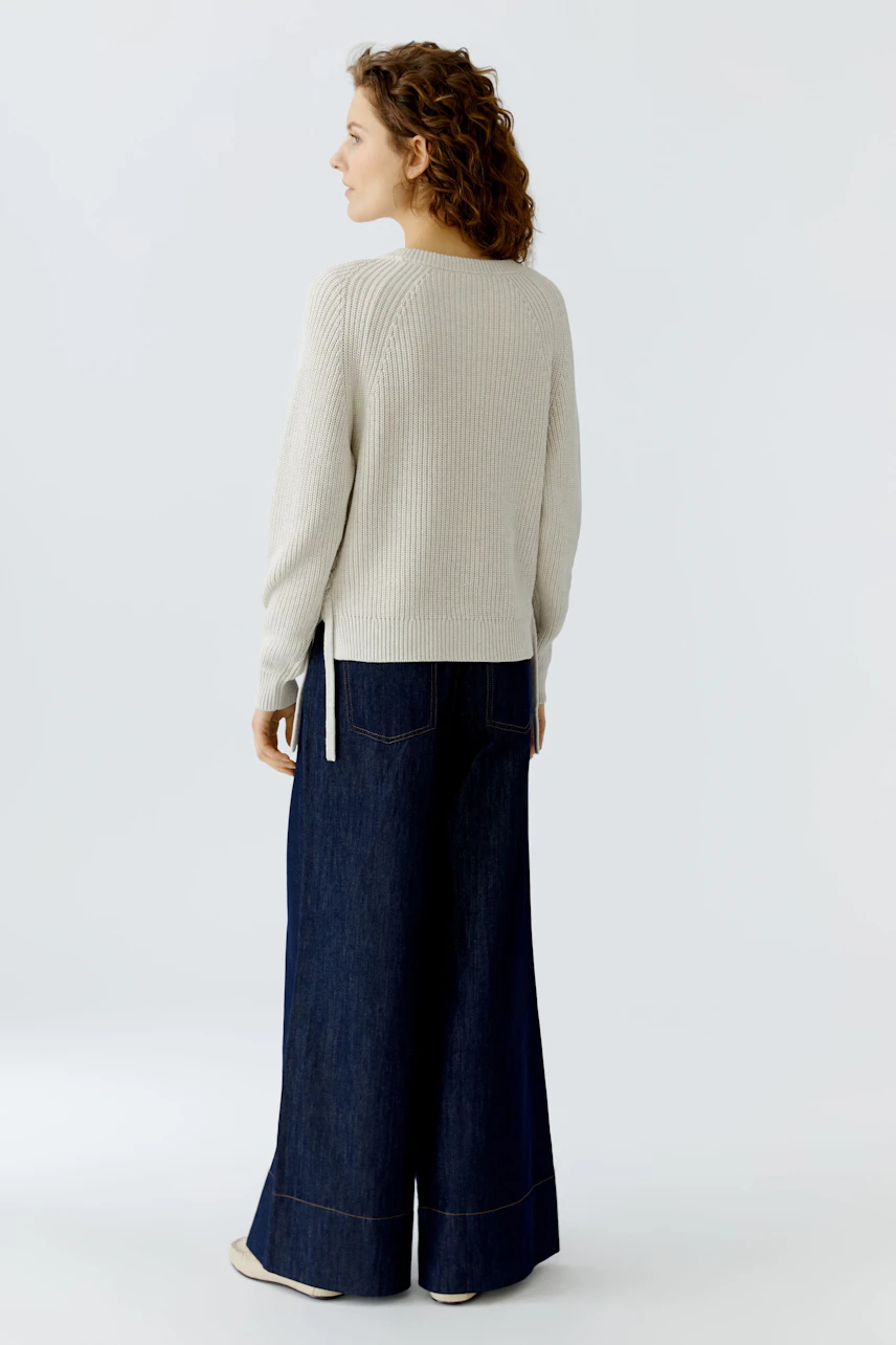 Casual women's pullover: A woman in a light gray ribbed pullover and wide-leg jeans, seen from the back.