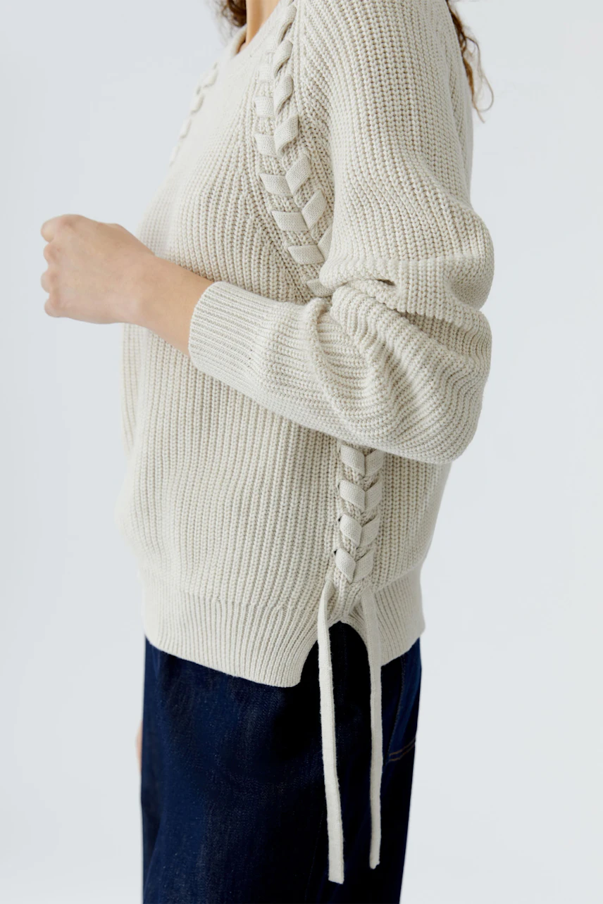 Casual women's pullover: A woman in a light beige knitted pullover with stylish side lacing.