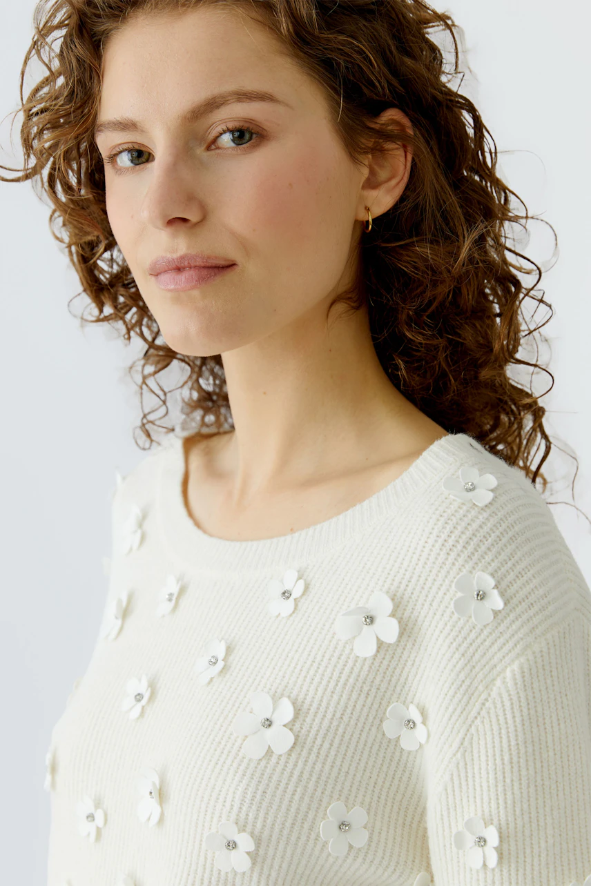 Damen-Pullover: Junge Frau in einem weißen Pullover mit Blumenapplikationen, lässig und modern.