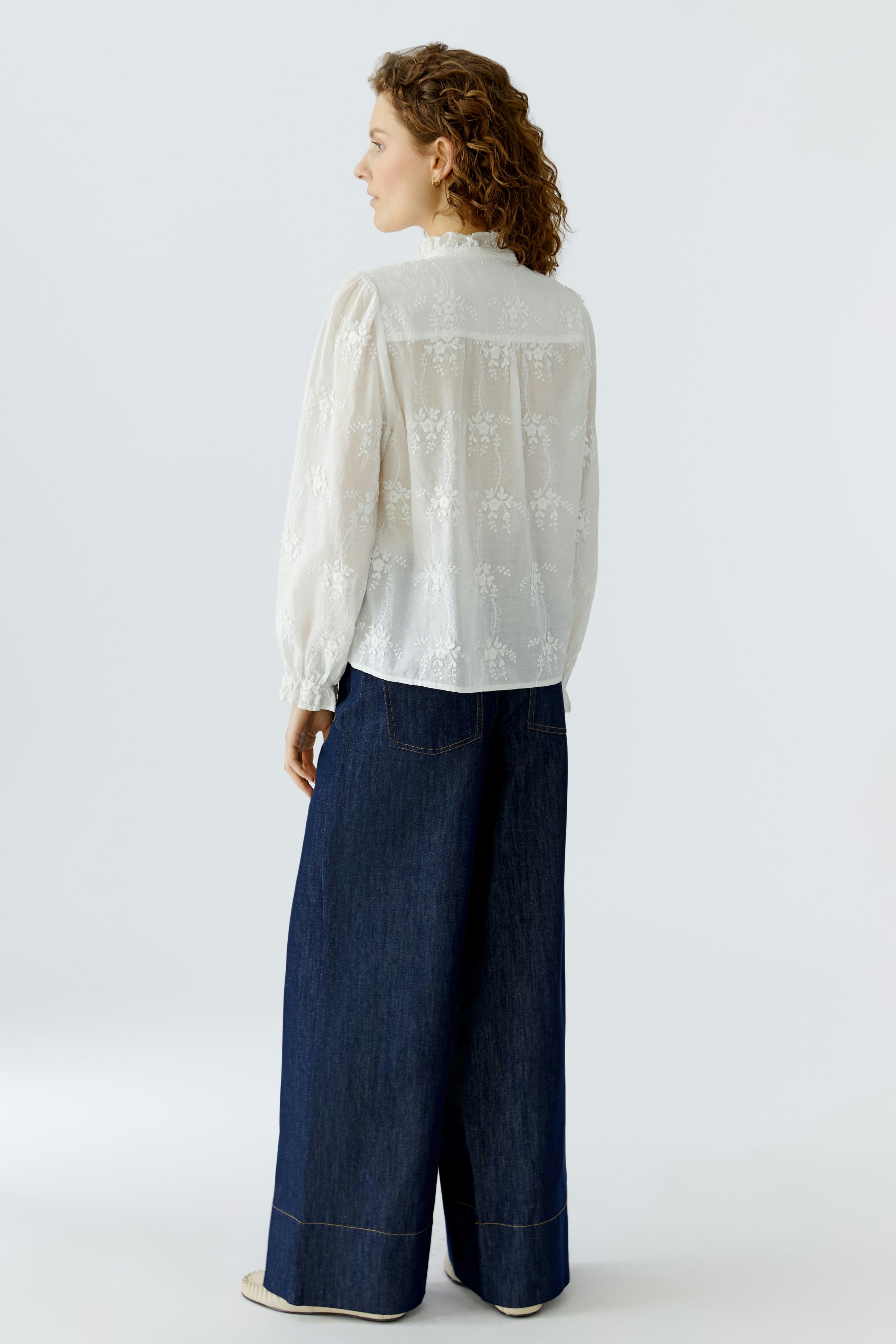 Light blouse: Woman in a sheer white blouse with floral details, paired with wide denim pants.