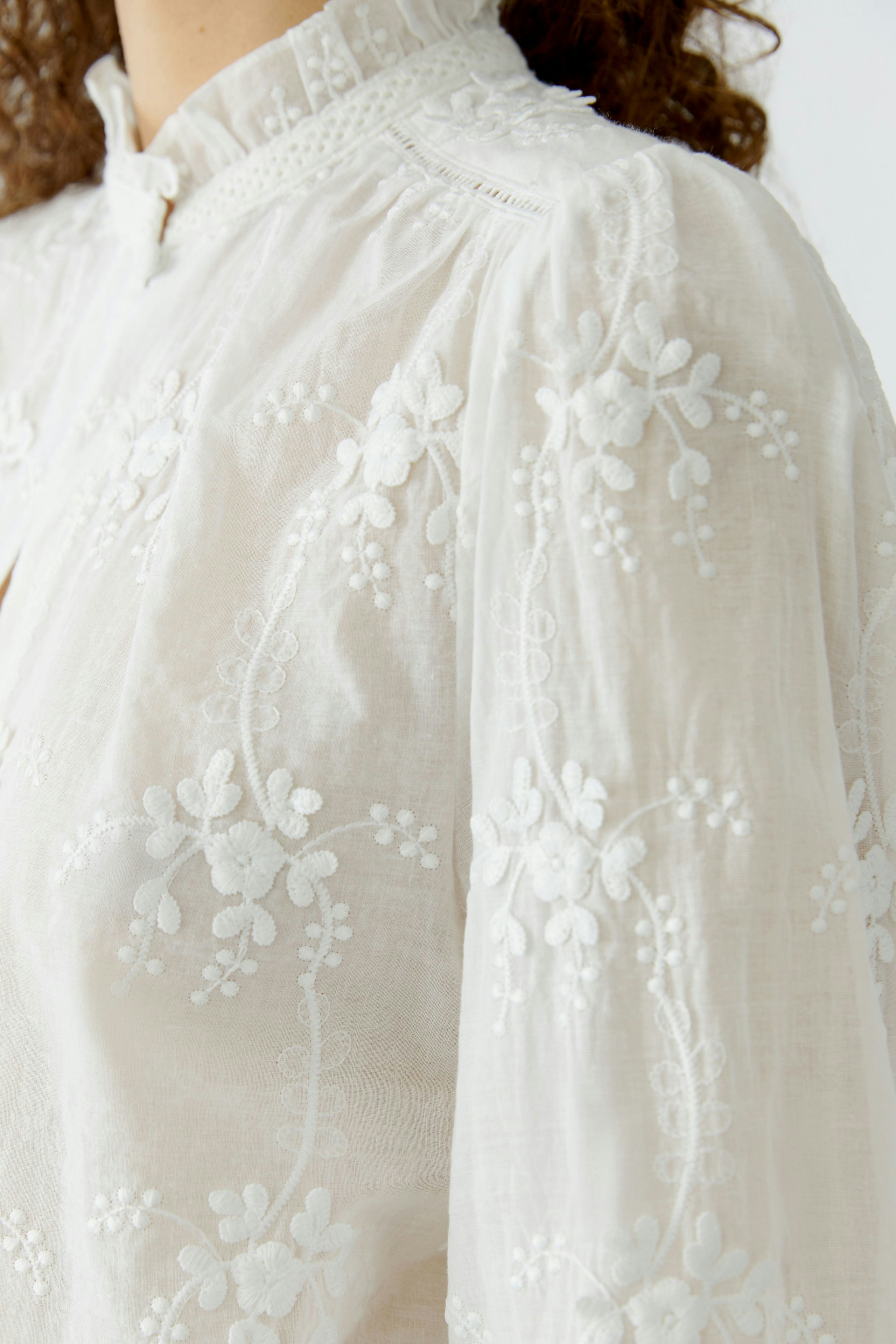 Lightweight women's blouse with floral embroidery, featuring a high neckline and puffed sleeves.