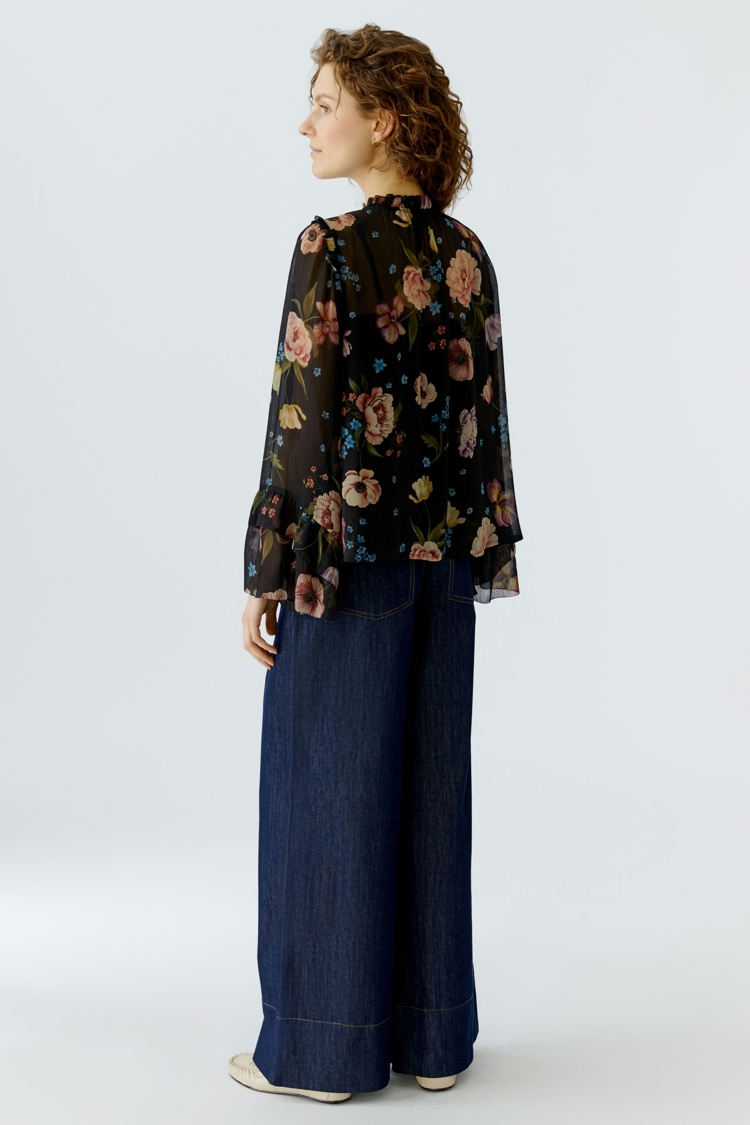Flowy blouse: Woman in a black floral blouse with ruffled sleeves, paired with wide-leg jeans.