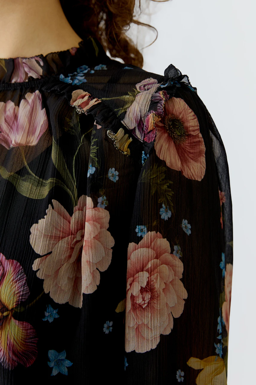 Floral blouse: Close-up of a woman's black blouse with colorful floral patterns and ruffled details.
