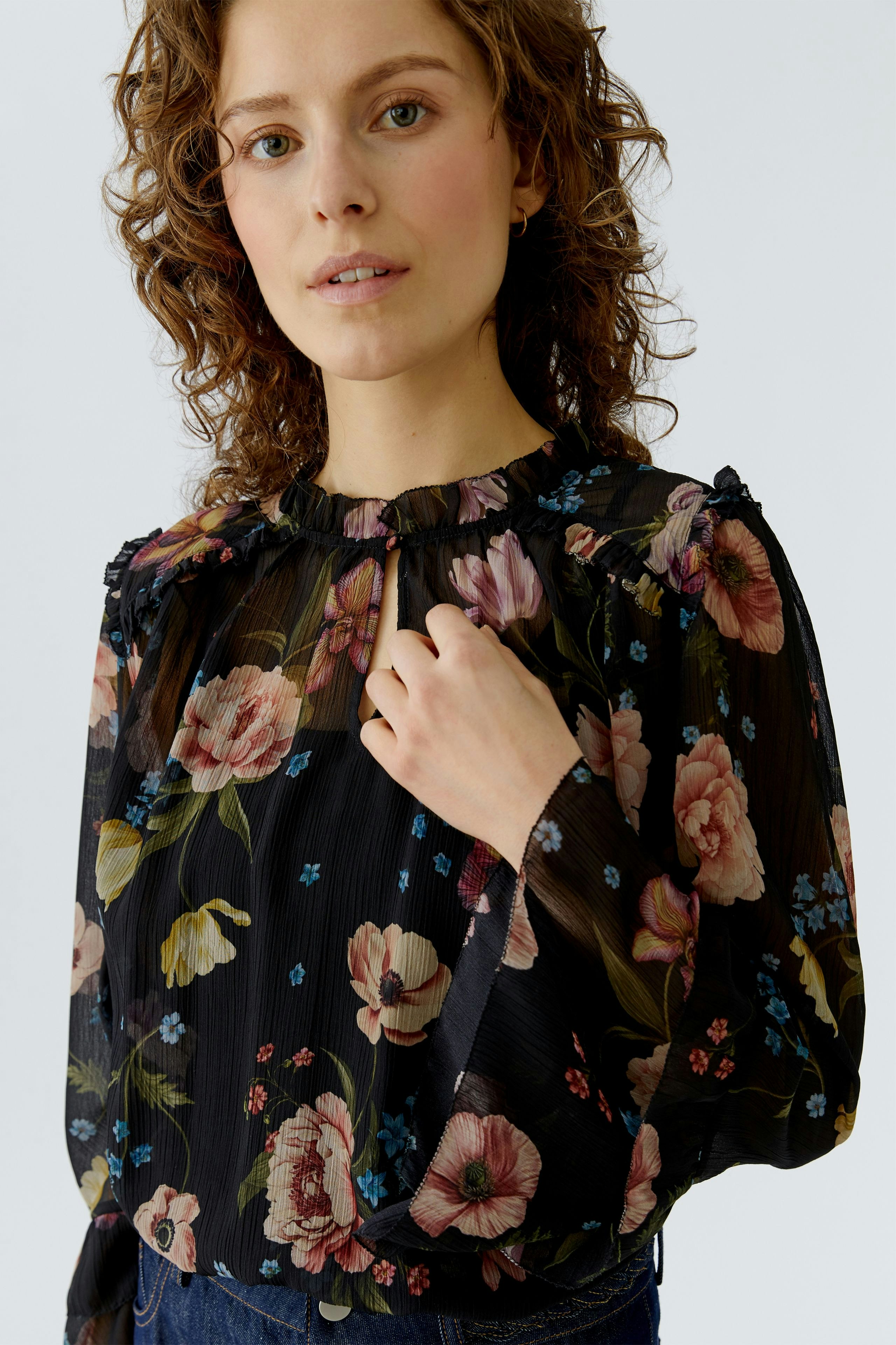 Floral blouse: Woman in a black blouse with colorful flowers, featuring a ruffled neckline and long sleeves.