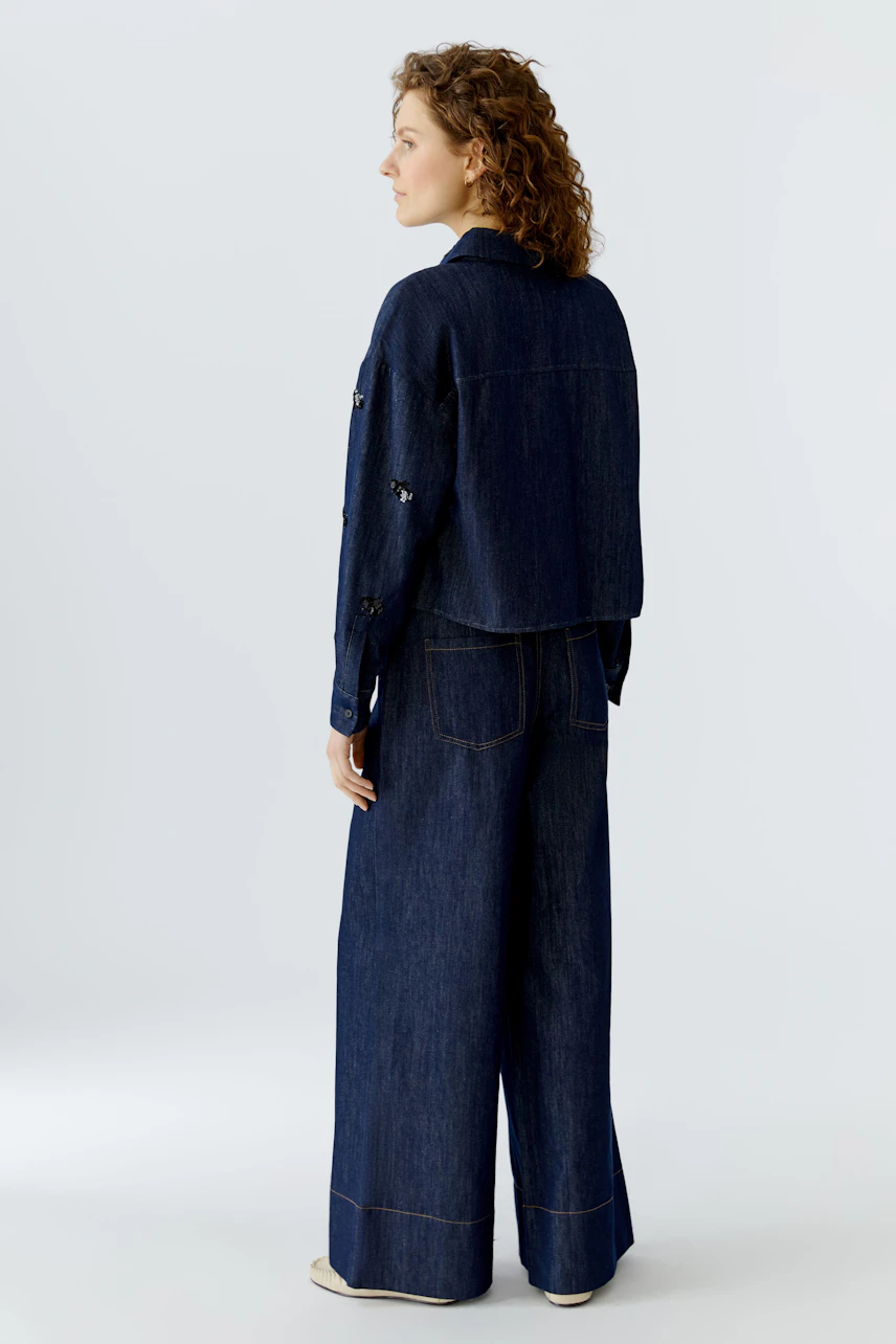 Damen-Jacke: Frau in blauer Jeansjacke mit lässigem Schnitt und dekorativen Details von hinten.