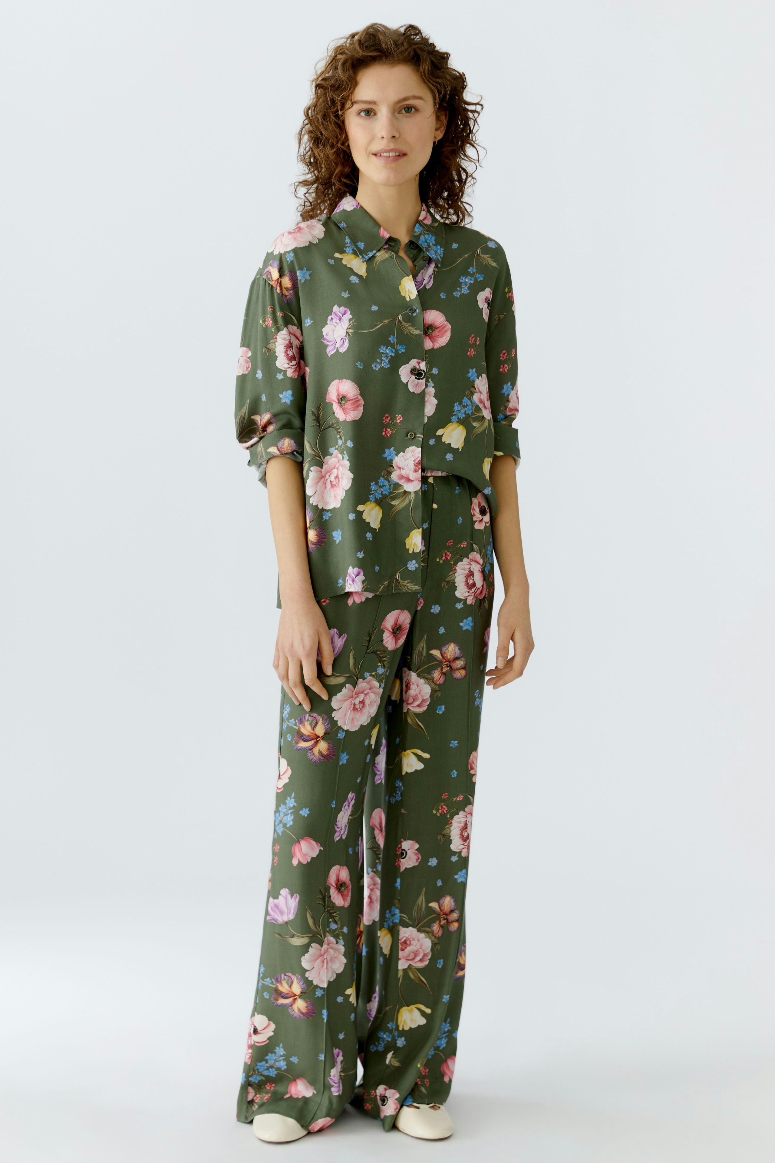 Floral blouse: Woman in a green floral blouse with matching pants, showcasing a relaxed style.