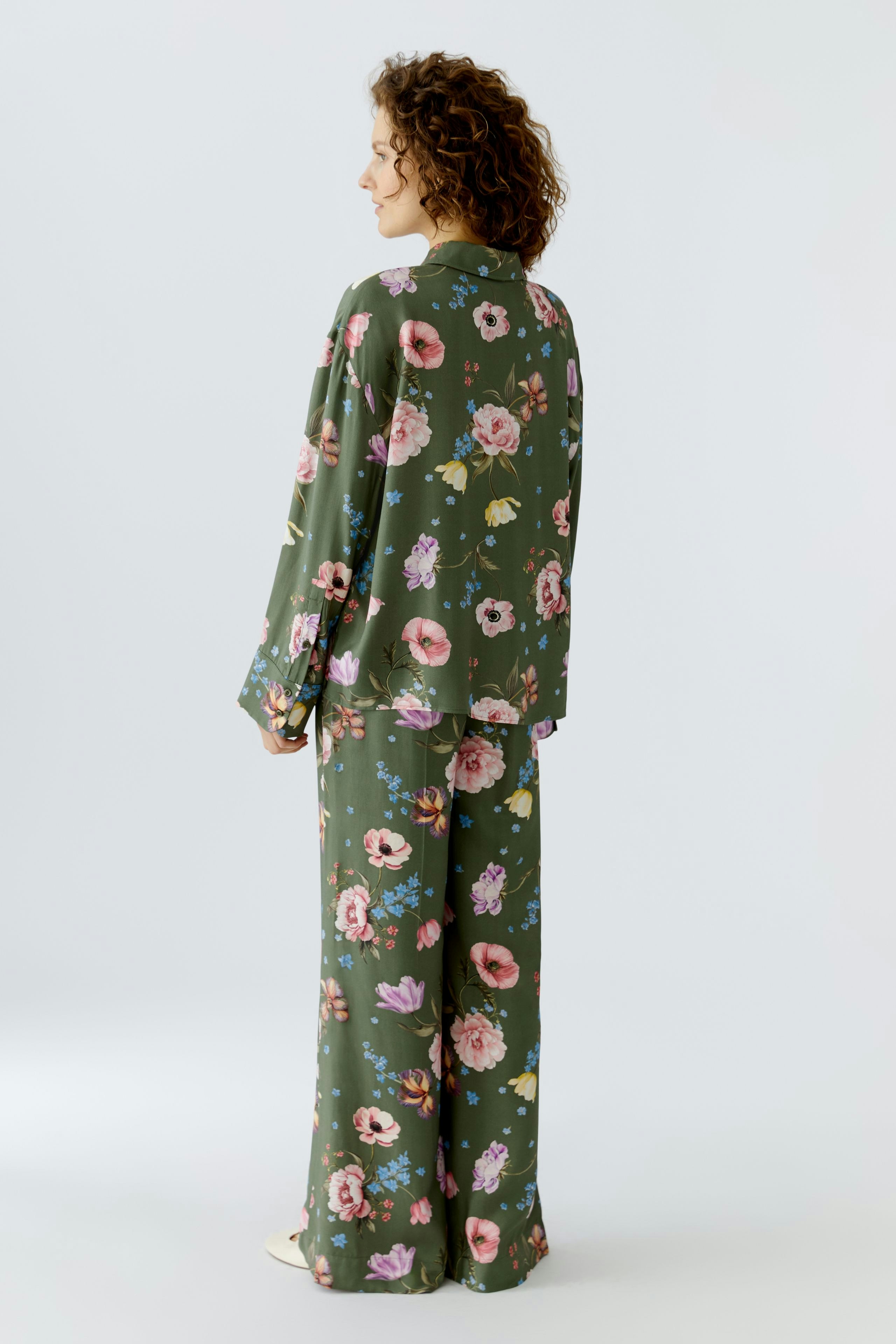 Floral blouse: Woman in a green floral blouse with matching pants, showcasing a relaxed style.