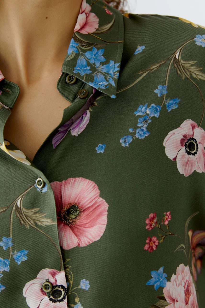 Bluse mit floralem Muster: Frau trägt eine grüne Bluse mit bunten Blumen und Knopfleiste.