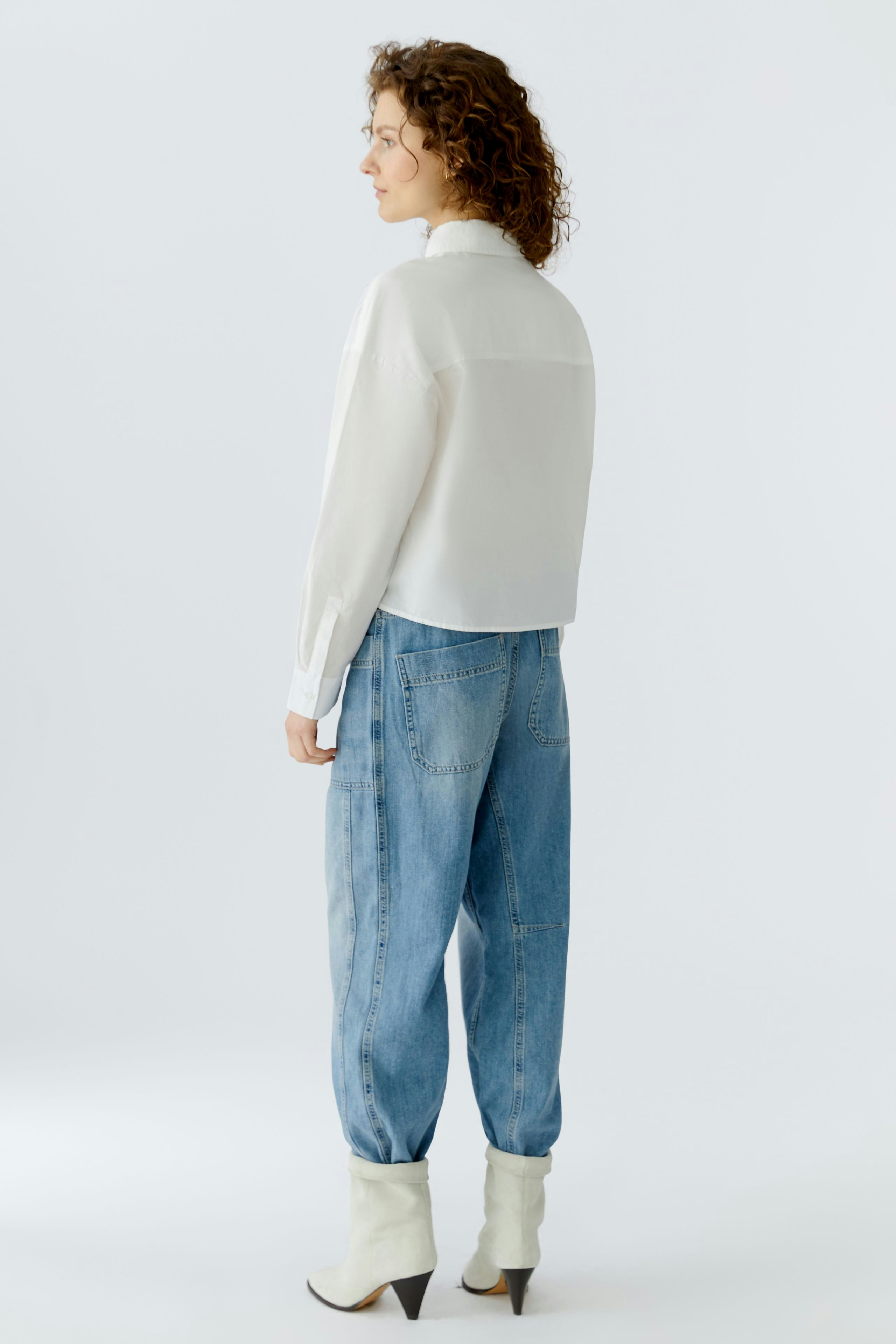 Casual women's blouse: A woman in a white blouse paired with relaxed denim pants, showcasing a modern look.