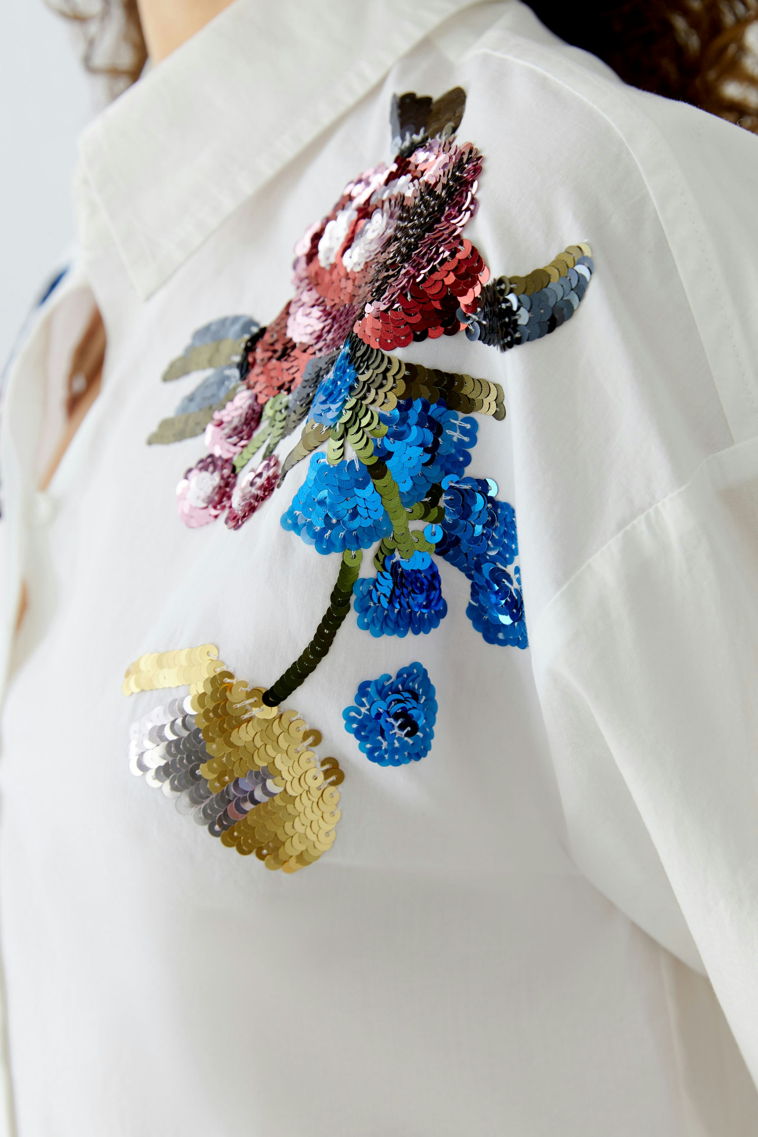 Casual women's blouse: Close-up of a woman wearing a white blouse with colorful sequin floral details.