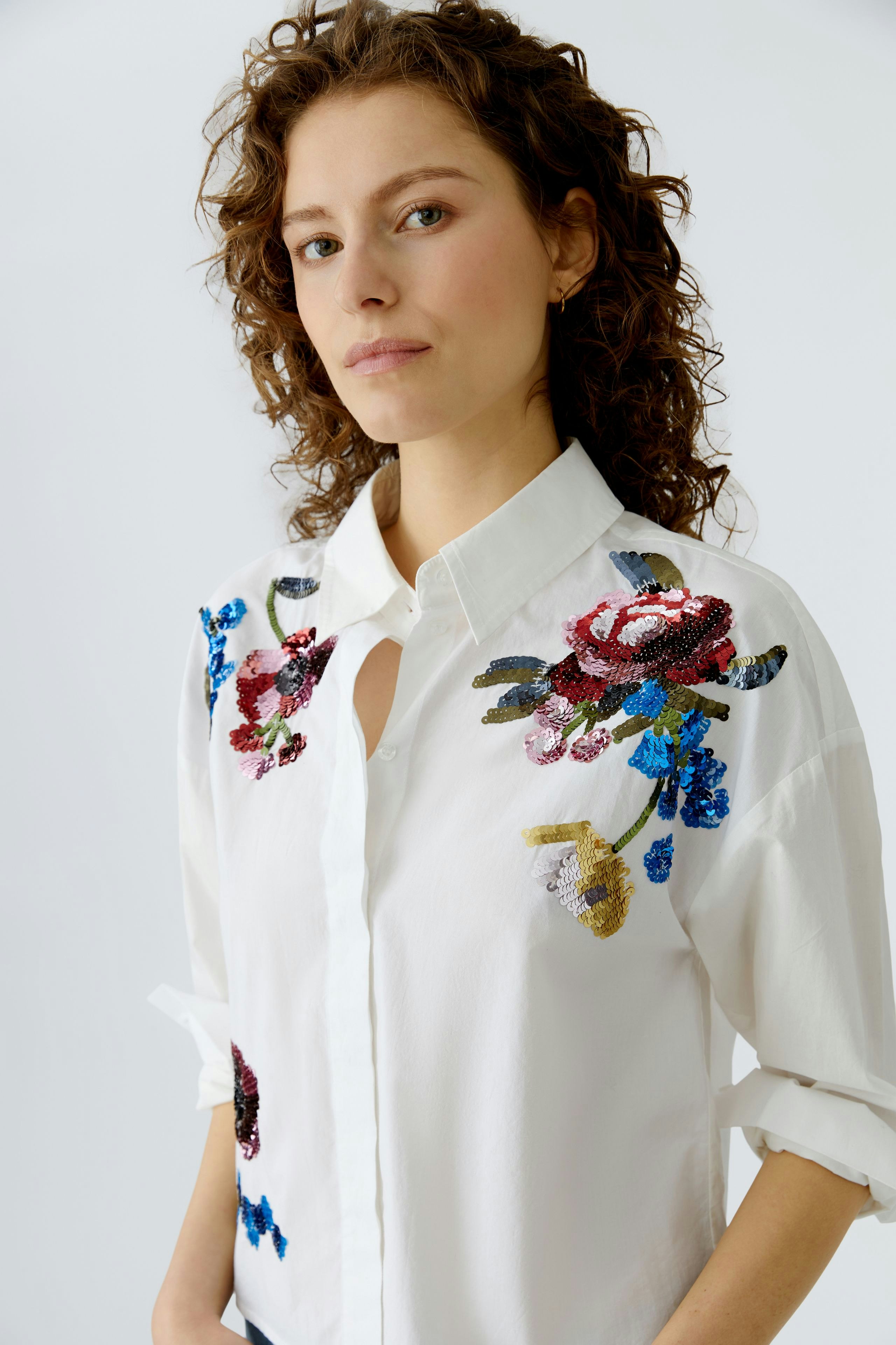 Stylish women's blouse: A woman in a white shirt with colorful floral embroidery, exuding a casual vibe.