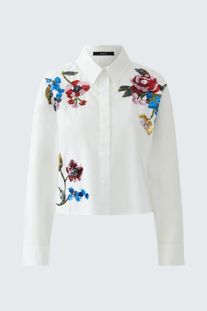 Cropped blouse: A woman in a white shirt with colorful floral embroidery, showcasing a casual style.