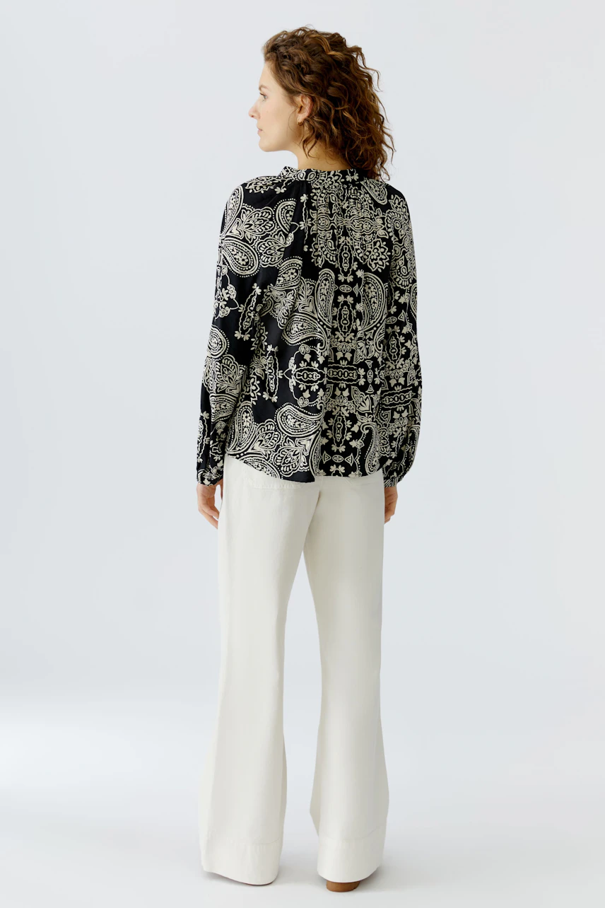 Stylish women's blouse: A woman in a patterned black and white blouse paired with light trousers.