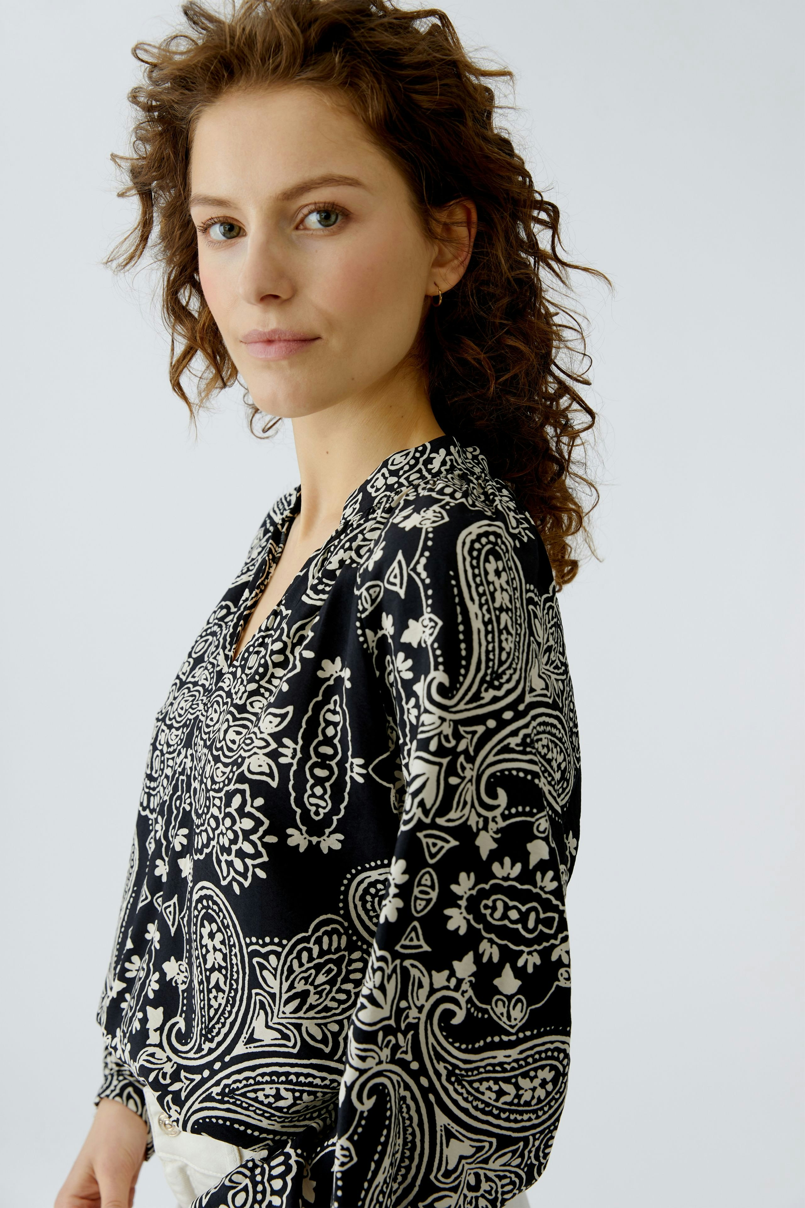 Damen-Bluse: Frau in schwarzer Bluse mit Paisleymuster, lässig und modern.