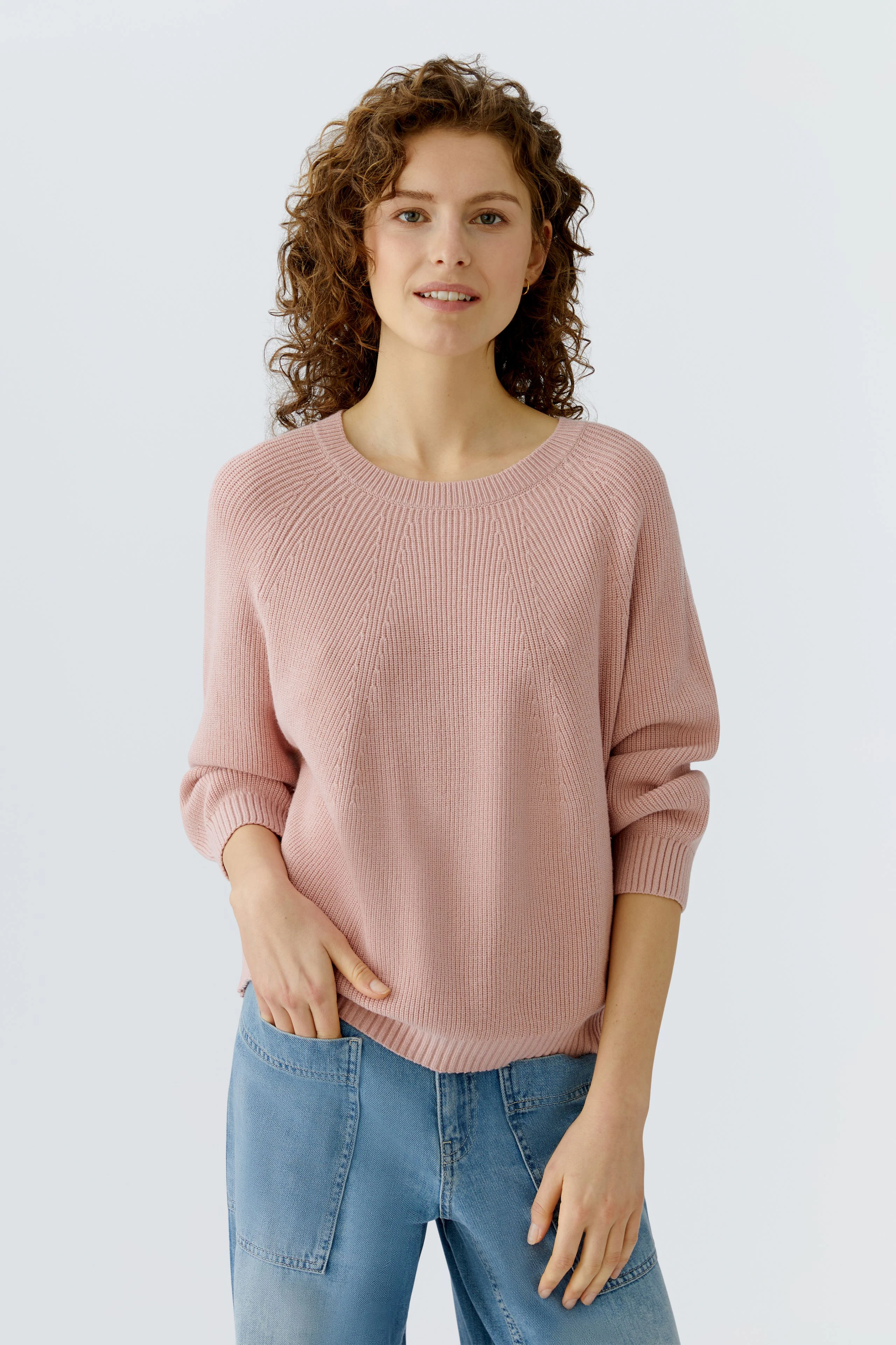 Damen-Pullover in zartem Rosa: Frau mit lockigem Haar trägt einen lässigen, bequemen Pullover.