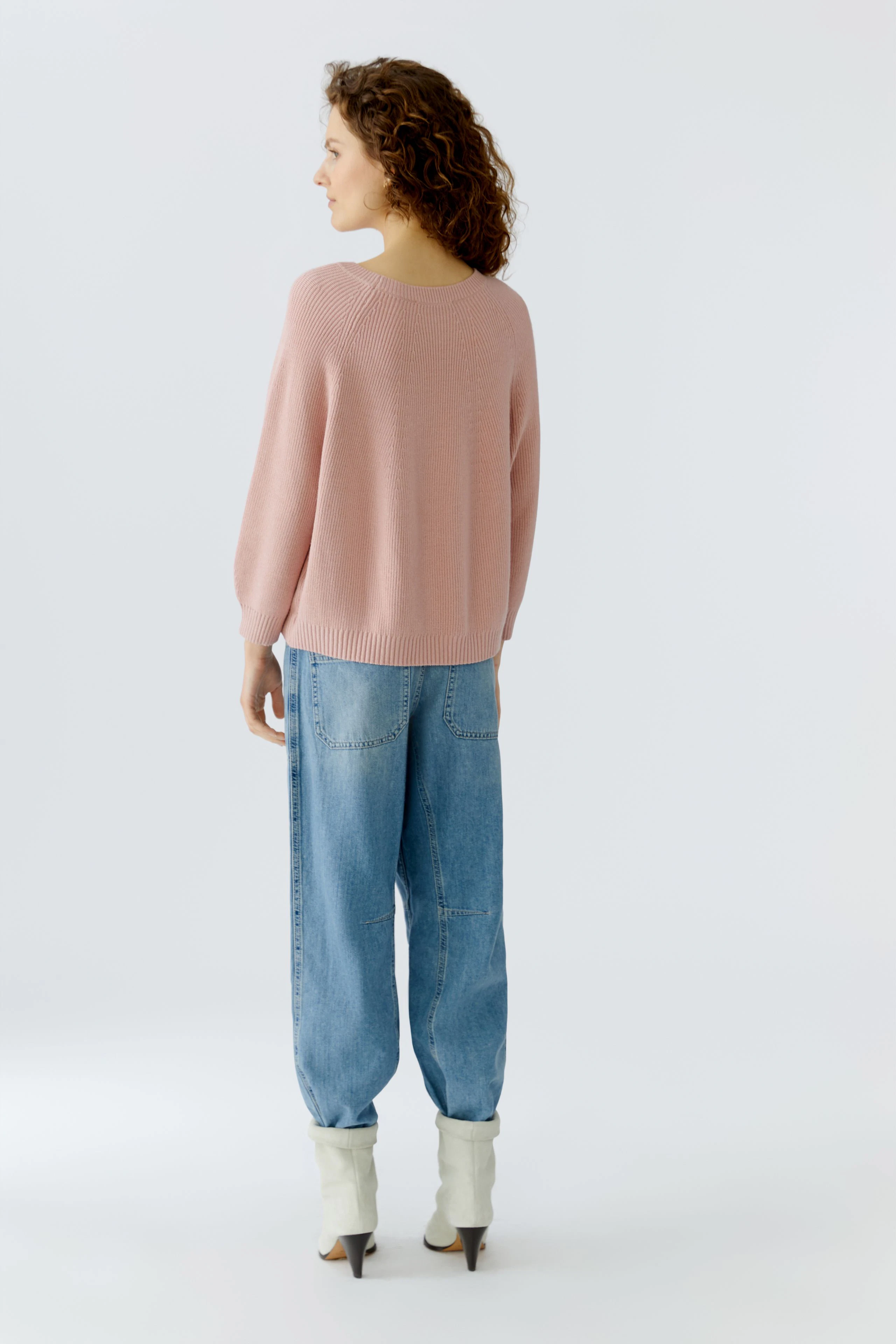 Damen-Pullover: Frau in rosafarbenem Strickpullover mit lockerer Passform und lässigen Jeans.