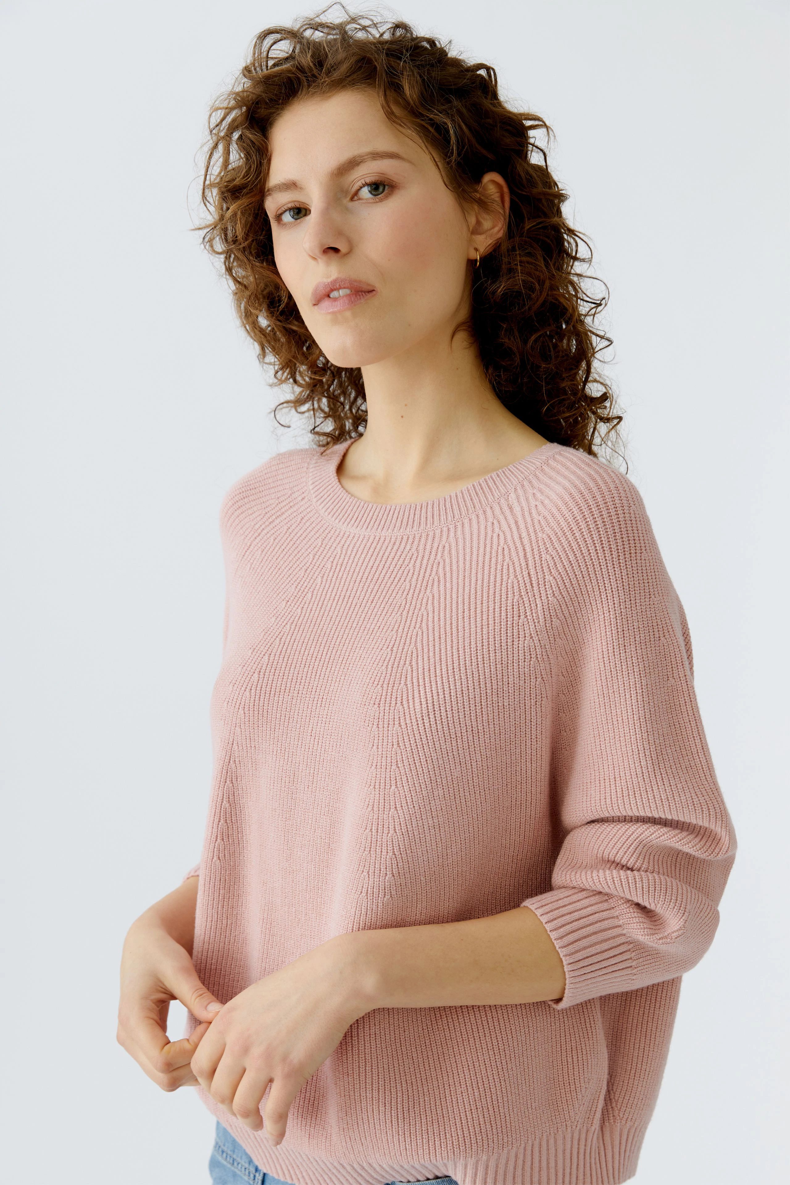Damen-Pullover: Junge Frau in einem rosafarbenen Strickpullover mit lässigem Schnitt und 3/4-Ärmeln.