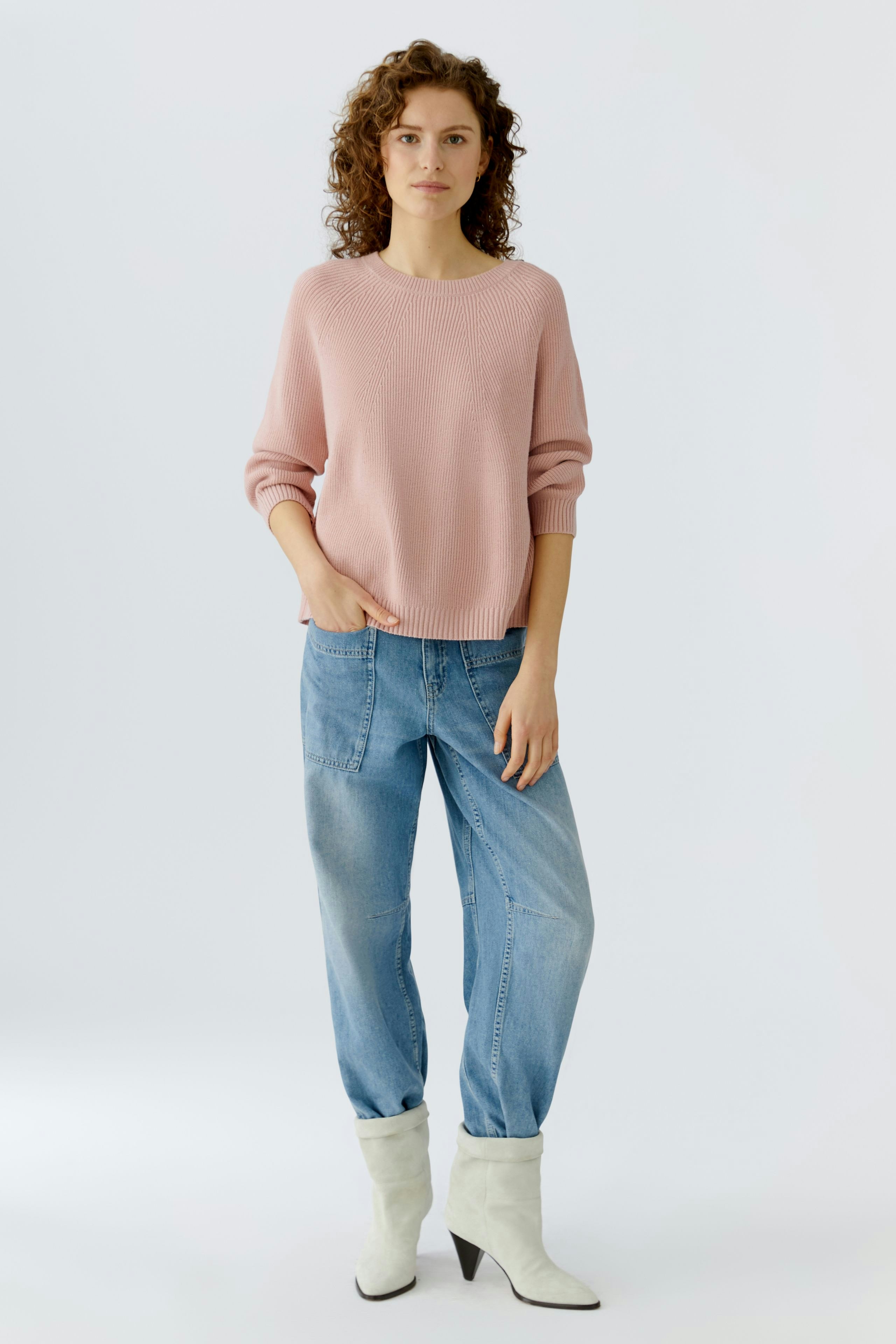 Casual women's pullover: Young woman in a light pink pullover paired with relaxed jeans and stylish boots.