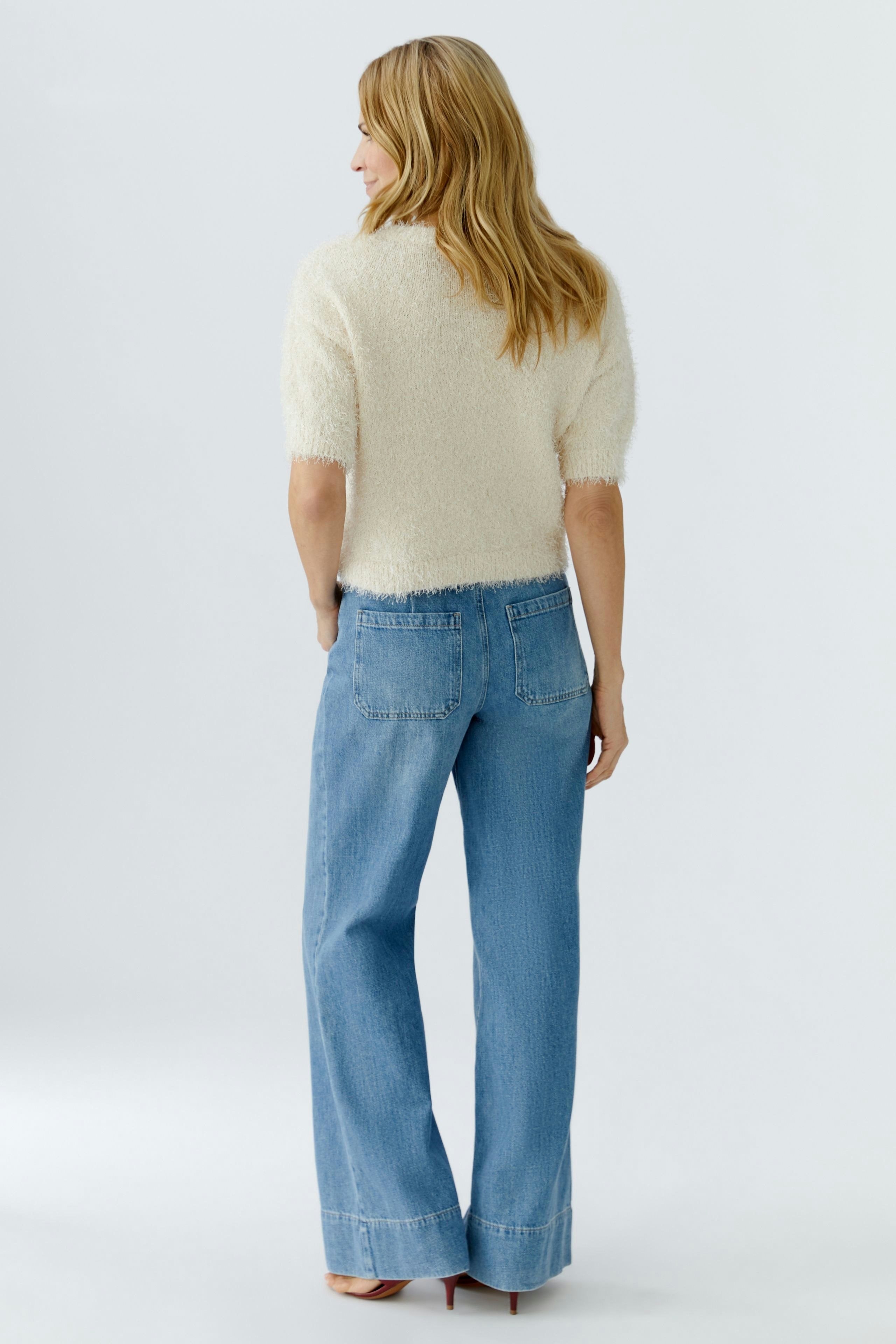 Casual women's pullover: A woman in a fluffy cream pullover paired with wide-leg jeans, seen from the back.