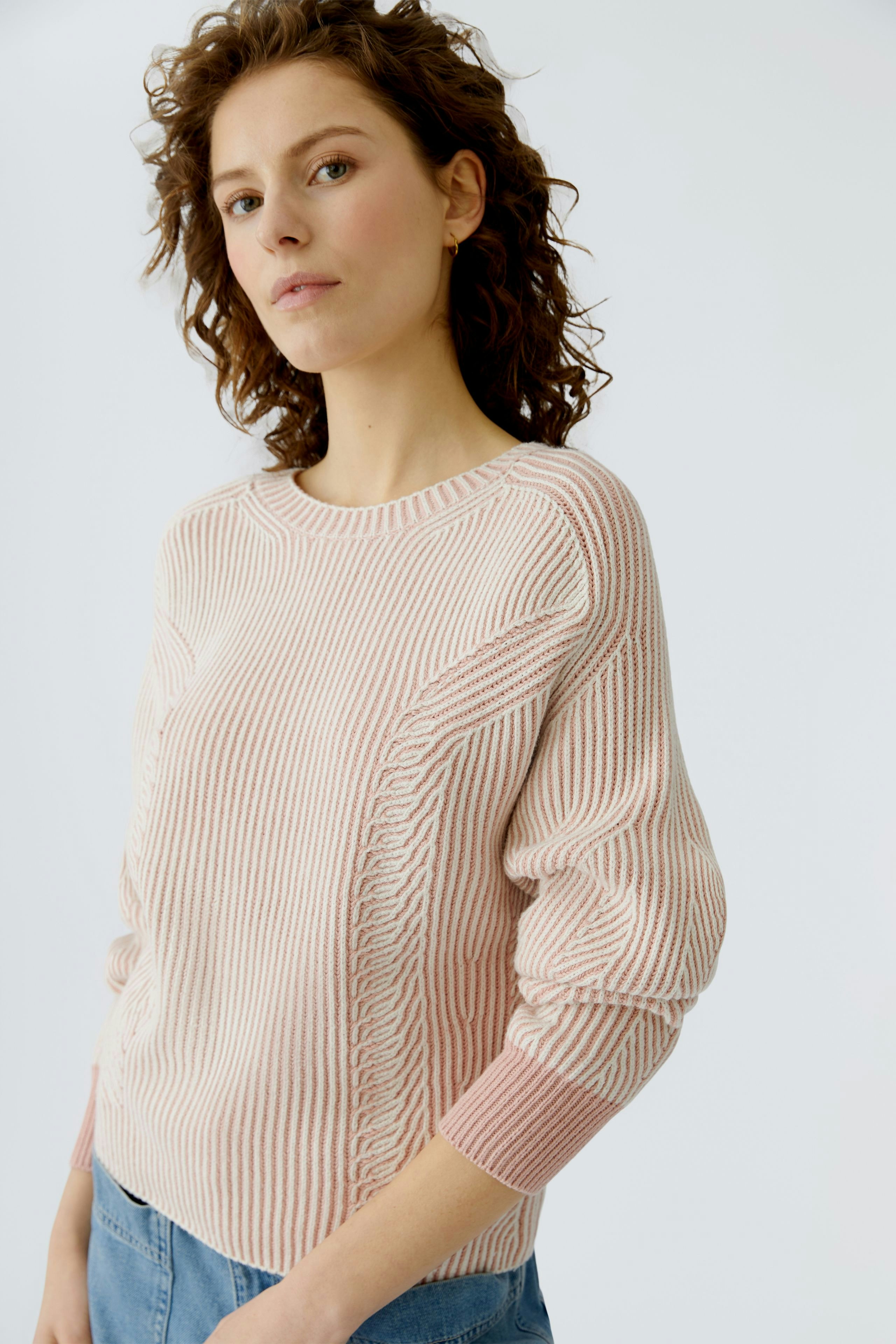 Casual women's pullover: Young woman in a pink striped pullover with relaxed fit and rolled sleeves.