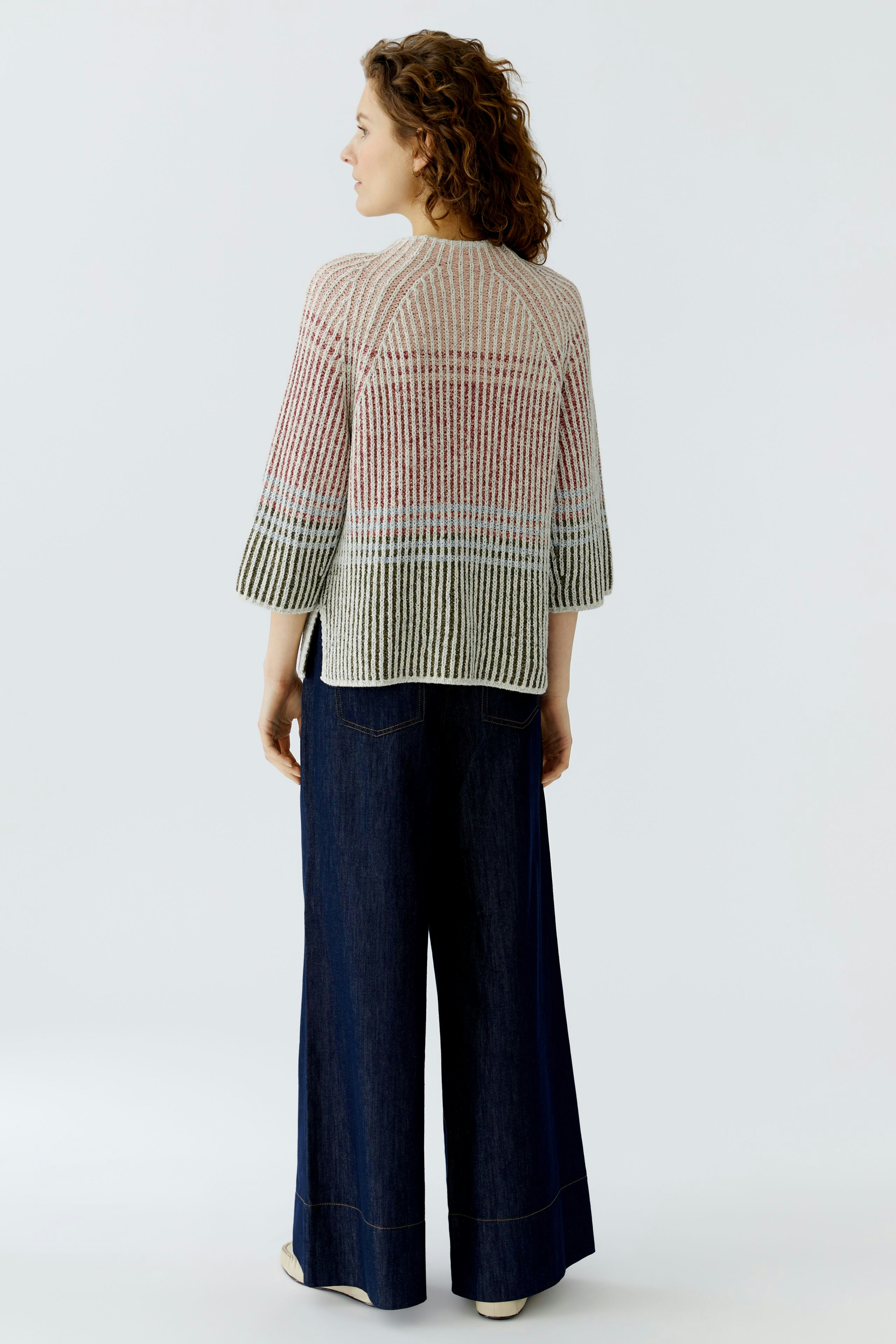 Casual women's pullover: A woman in a colorful knitted pullover with wide sleeves, paired with denim pants.