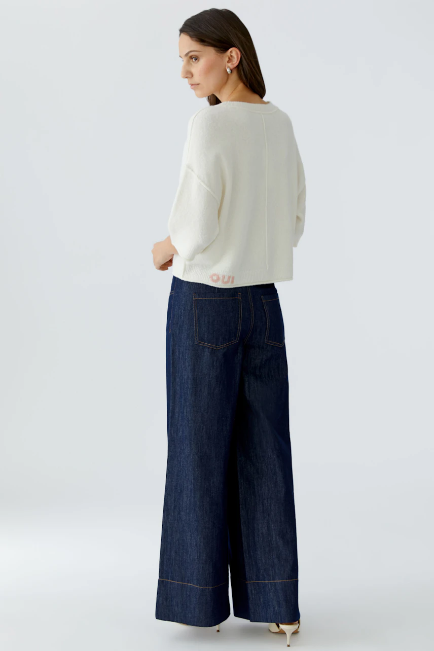 Casual women's pullover: A woman in a light pullover with wide sleeves and relaxed fit, paired with denim.
