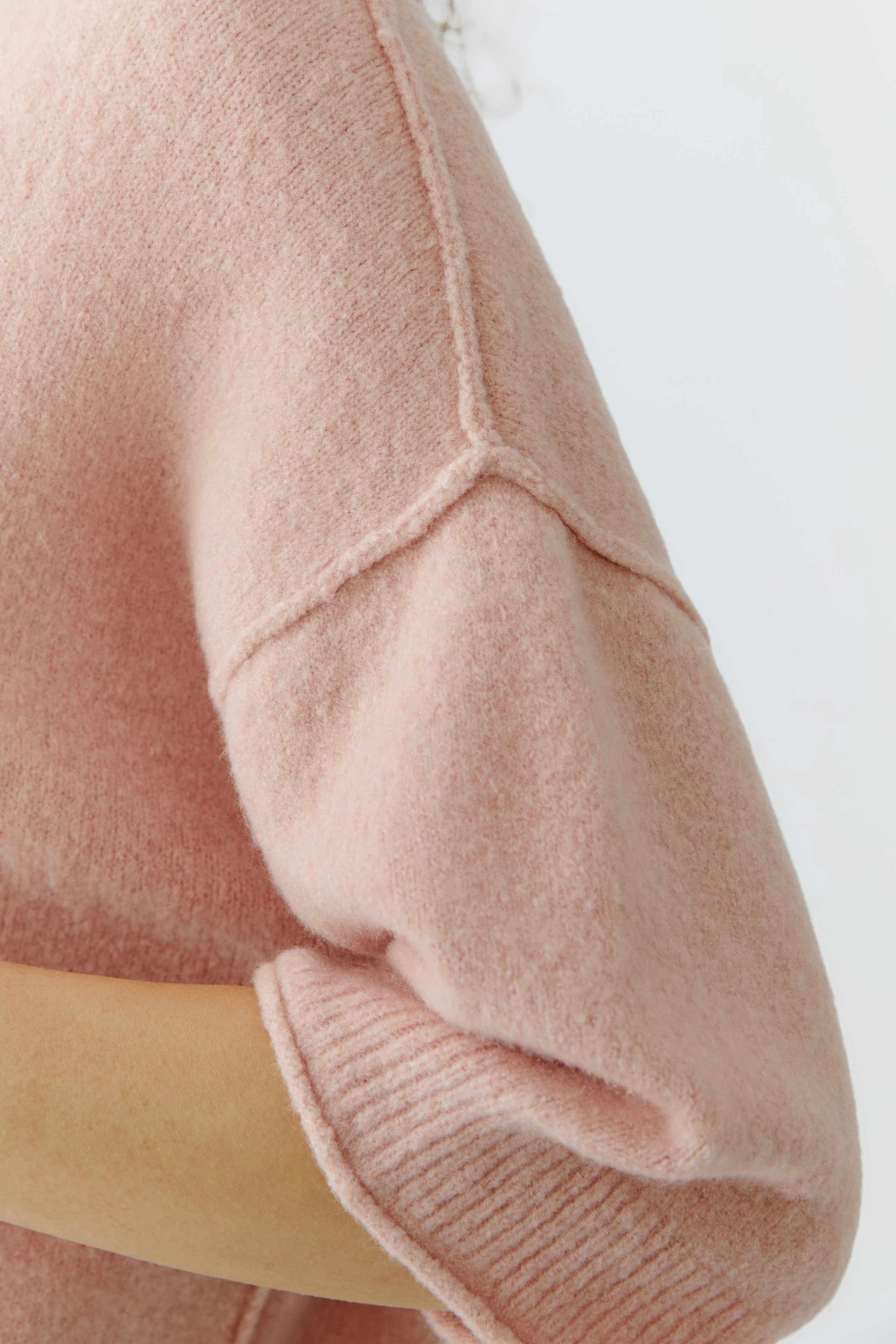 Soft pink pullover: Close-up of a woman's cozy pullover with rolled sleeves and a relaxed fit.