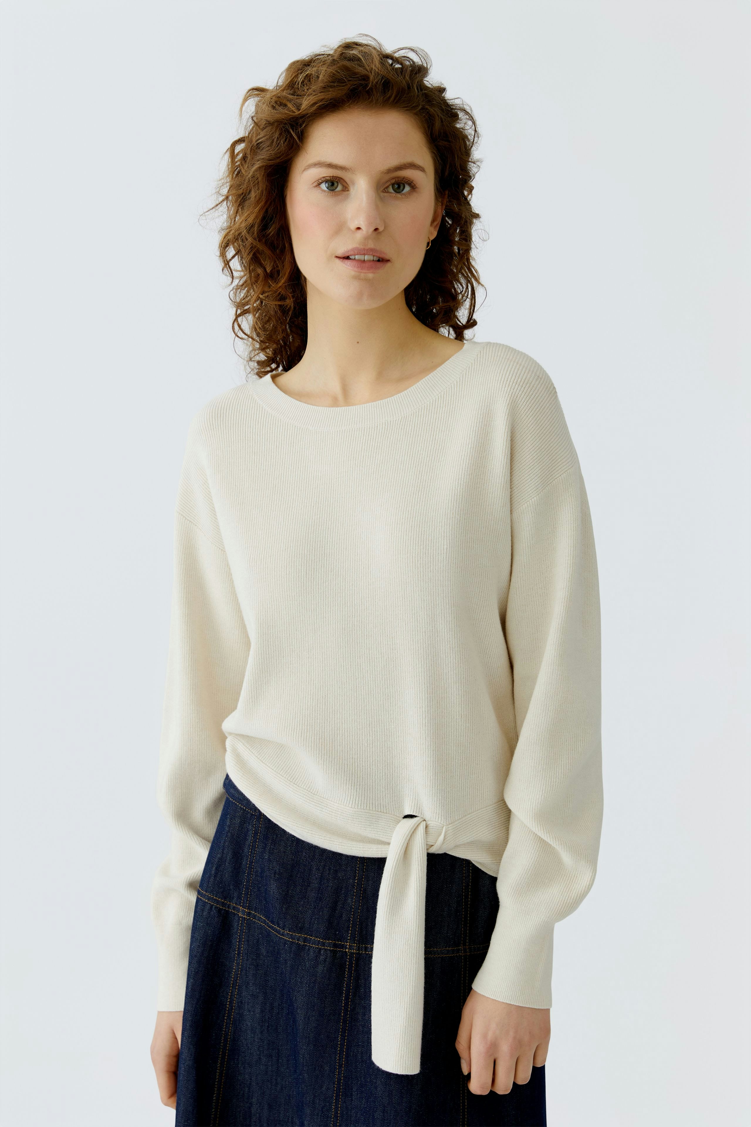 Casual women's pullover: A woman in a light beige pullover with a tied detail, paired with a denim skirt.