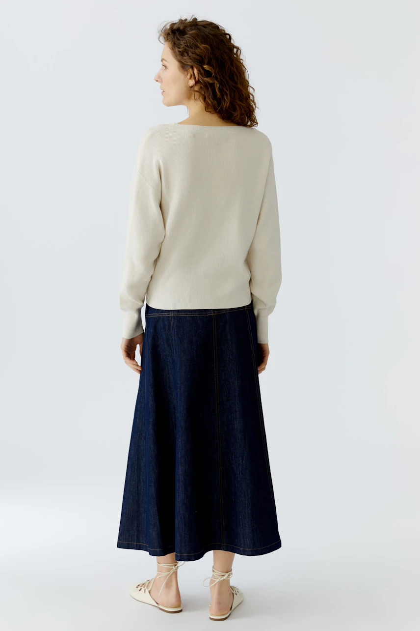 Casual women's pullover: A woman in a cream pullover paired with a long denim skirt, viewed from the back.