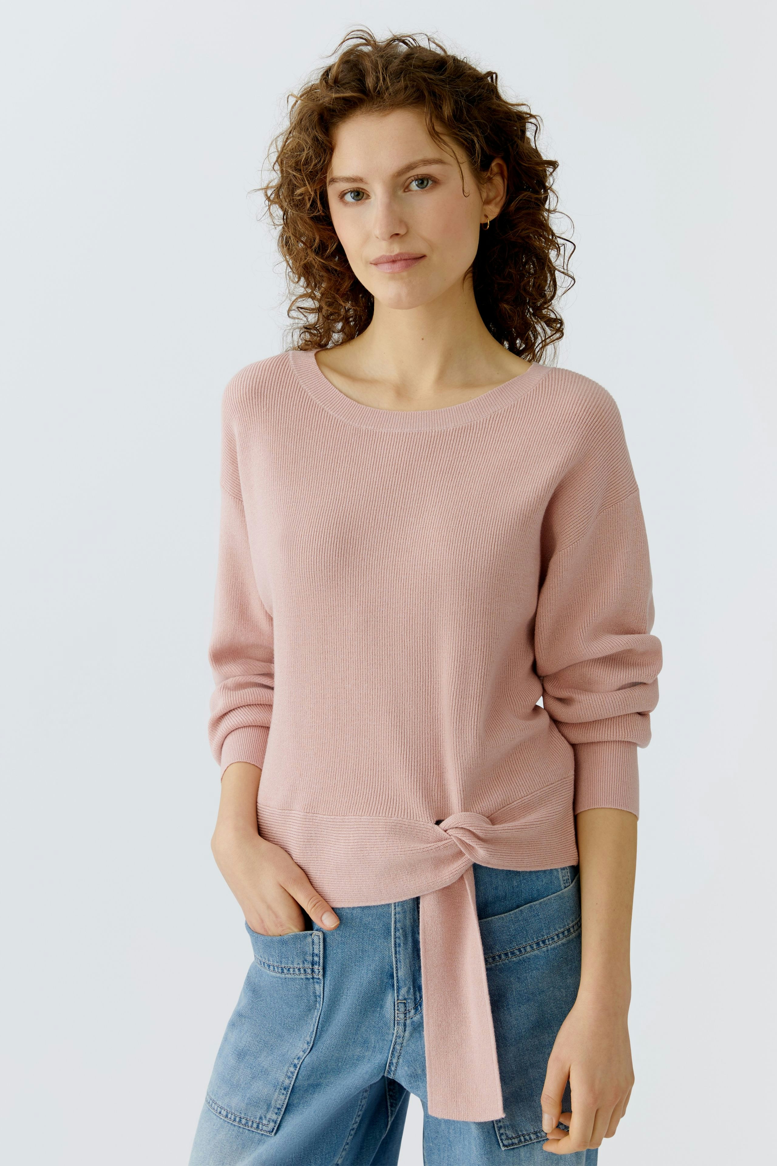 Casual women's pullover: Young woman in a light pink pullover with a knot detail, paired with denim.